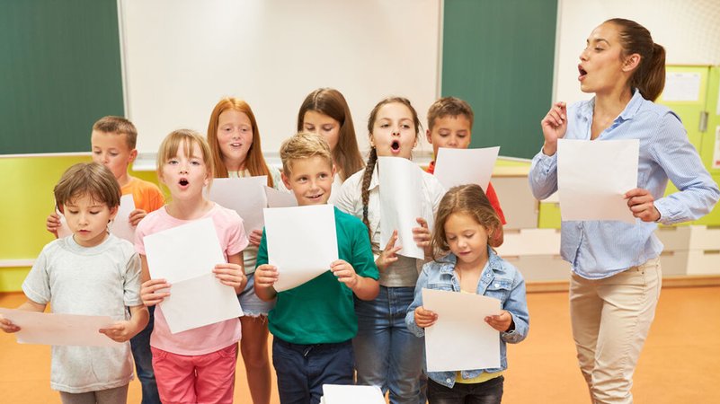 (Symbolbild) Grundschulkinder singen gemeinsam mit ihrer Lehrerin im Chor in einem Klassenzimmer. | Bild: stock.adobe.com/Robert Kneschke (Symbolbild) Grundschulkinder singen gemeinsam mit ihrer Lehrerin im Chor in einem Klassenzimmer.