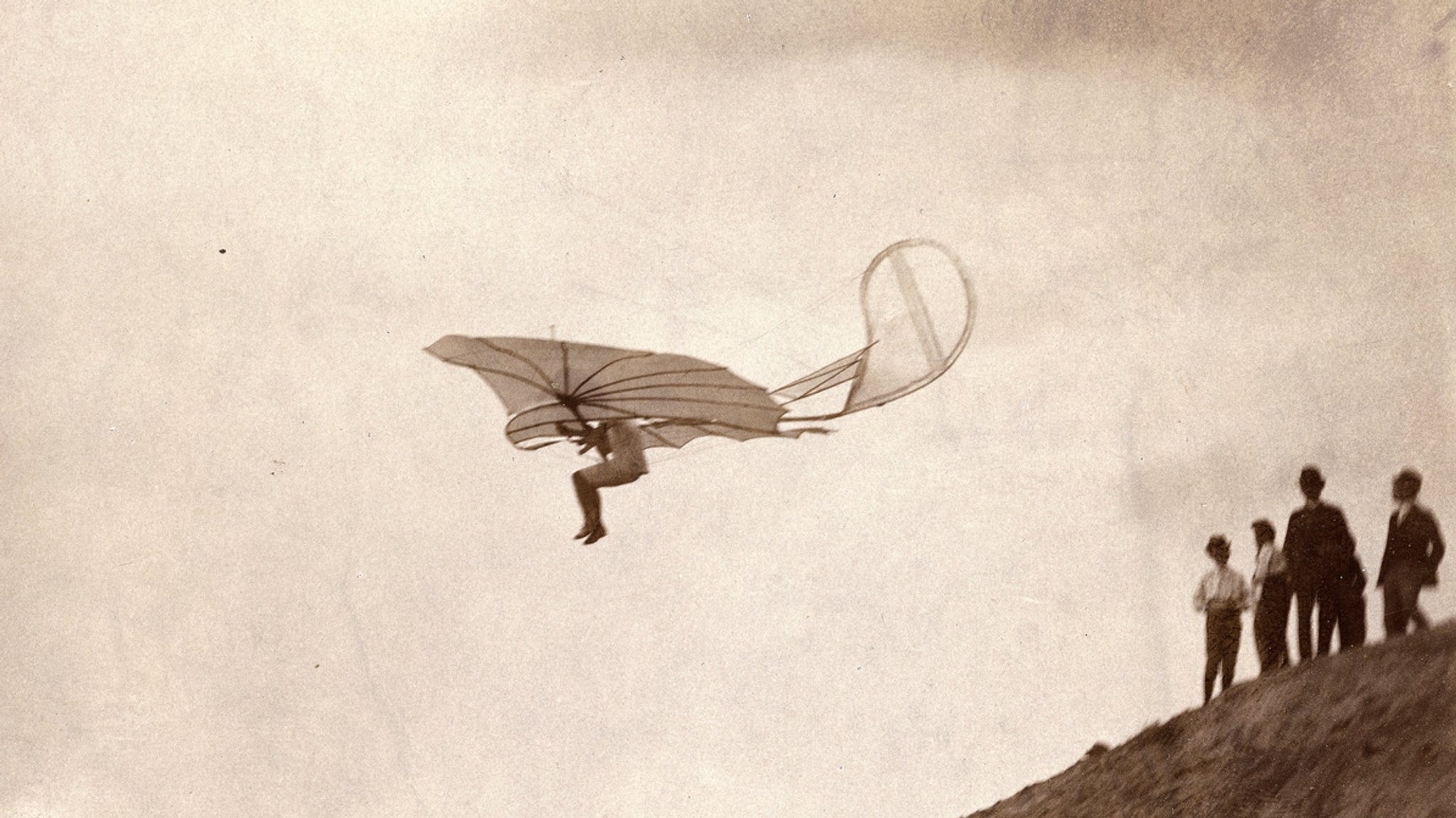 Menschen schauen Otto Lilienthal zu, wie er einen Hang hinabgleitet