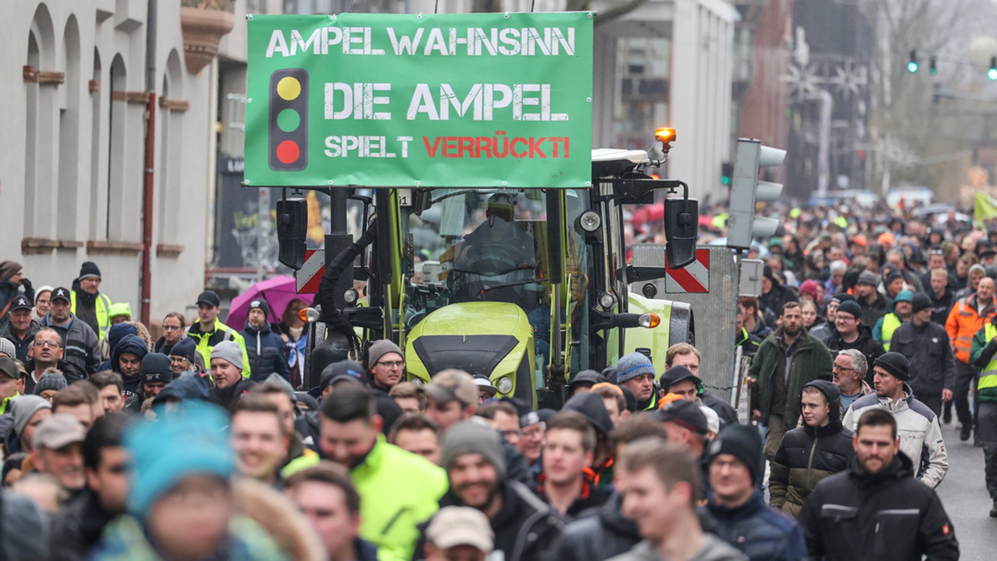 Teilnehmer einer Protestaktion gehen neben einem Traktor, an dem ein Schild "Ampel-Wahnsinn - die Ampel spielt verrückt!" angebracht ist. 