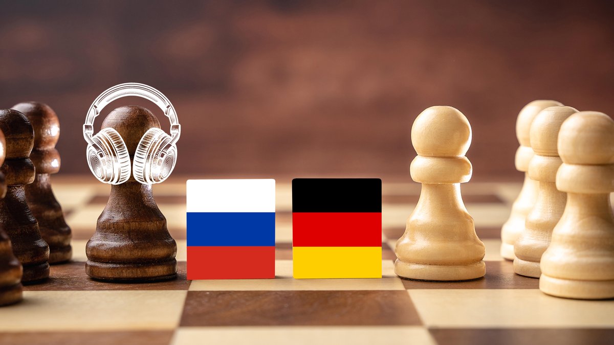Bildmontage eines Schachbretts mit weißen und schwarzen Figuren, getrennt durch die russische und deutsche Flagge. Eine Figur auf der Seite der russischen Flagge trägt Kopfhörer.