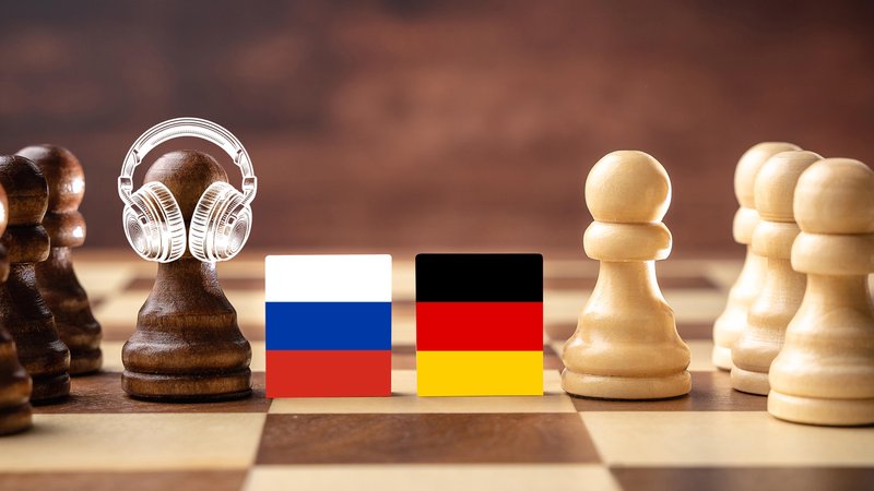 Bildmontage eines Schachbretts mit weißen und schwarzen Figuren, getrennt durch die russische und deutsche Flagge. Eine Figur auf der Seite der russischen Flagge trägt Kopfhörer.