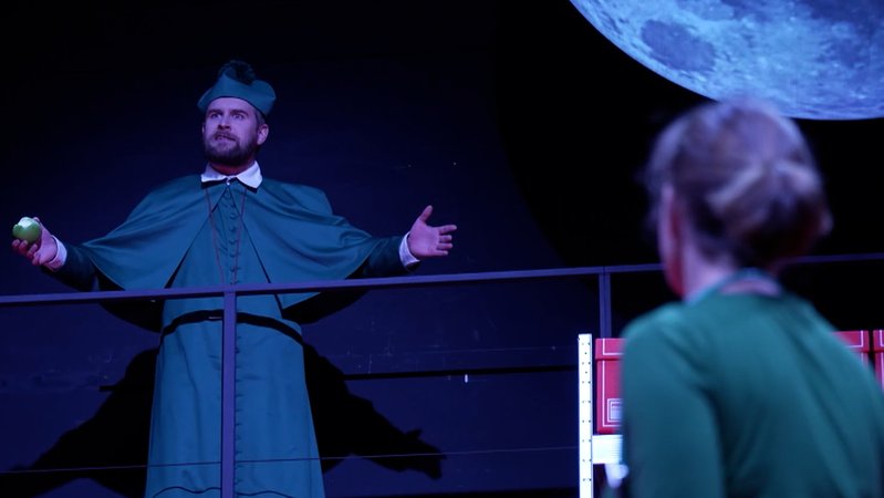 Ein Schauspieler im Talar eines Priesters, steht auf der Bühne und breitet die Arme aus. Vor ihm steht eine Frau im grünen Kleid. | Bild: BR Ein Schauspieler im Talar eines Priesters, steht auf der Bühne und breitet die Arme aus. Vor ihm steht eine Frau im grünen Kleid.