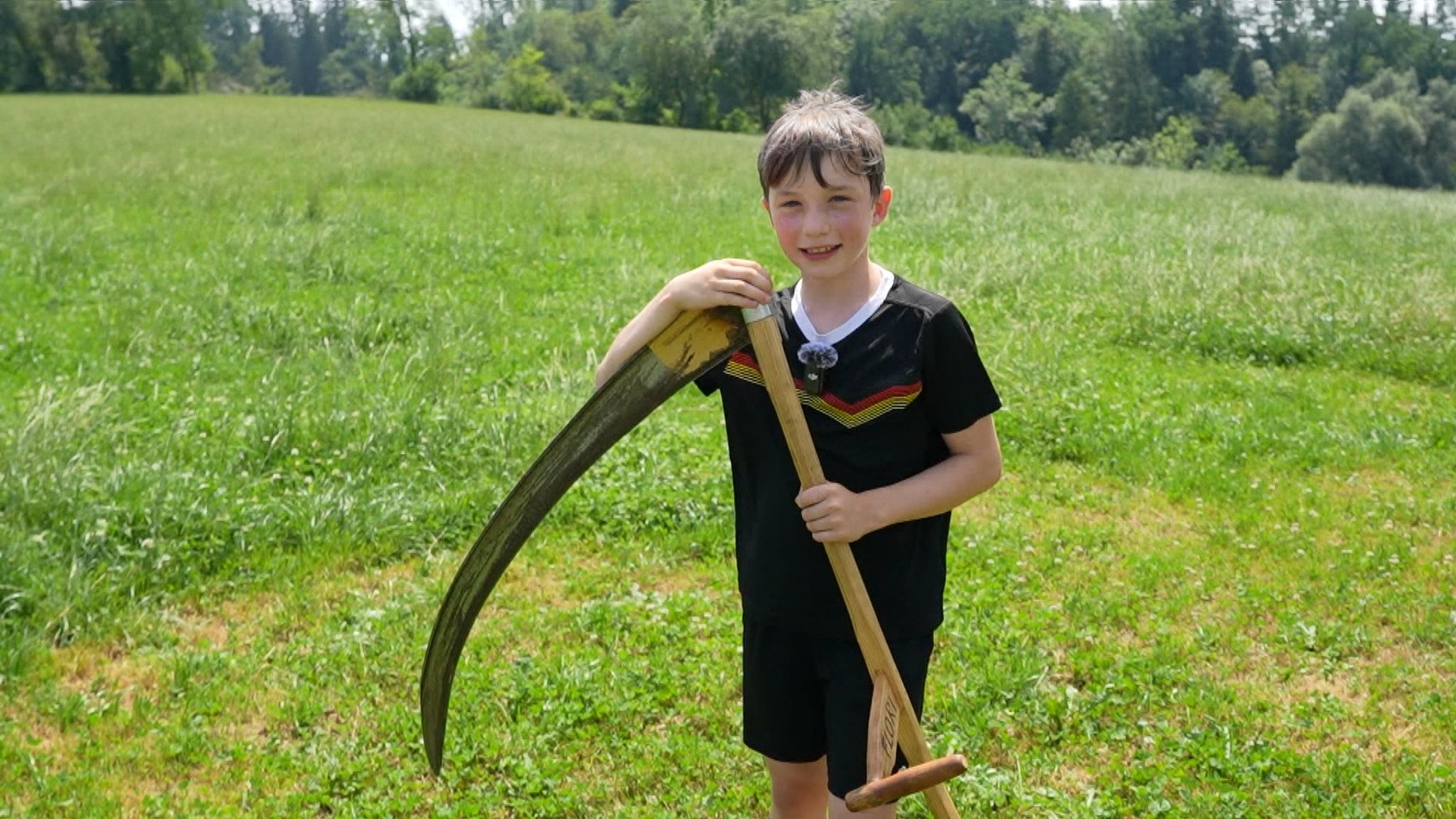 Der elfjährige Florian Linhart mit einer Sense auf einer teilweise gemähten Wiese. | Bild: BR / Stéphanie Mercier Der elfjährige Florian Linhart mit einer Sense auf einer teilweise gemähten Wiese.