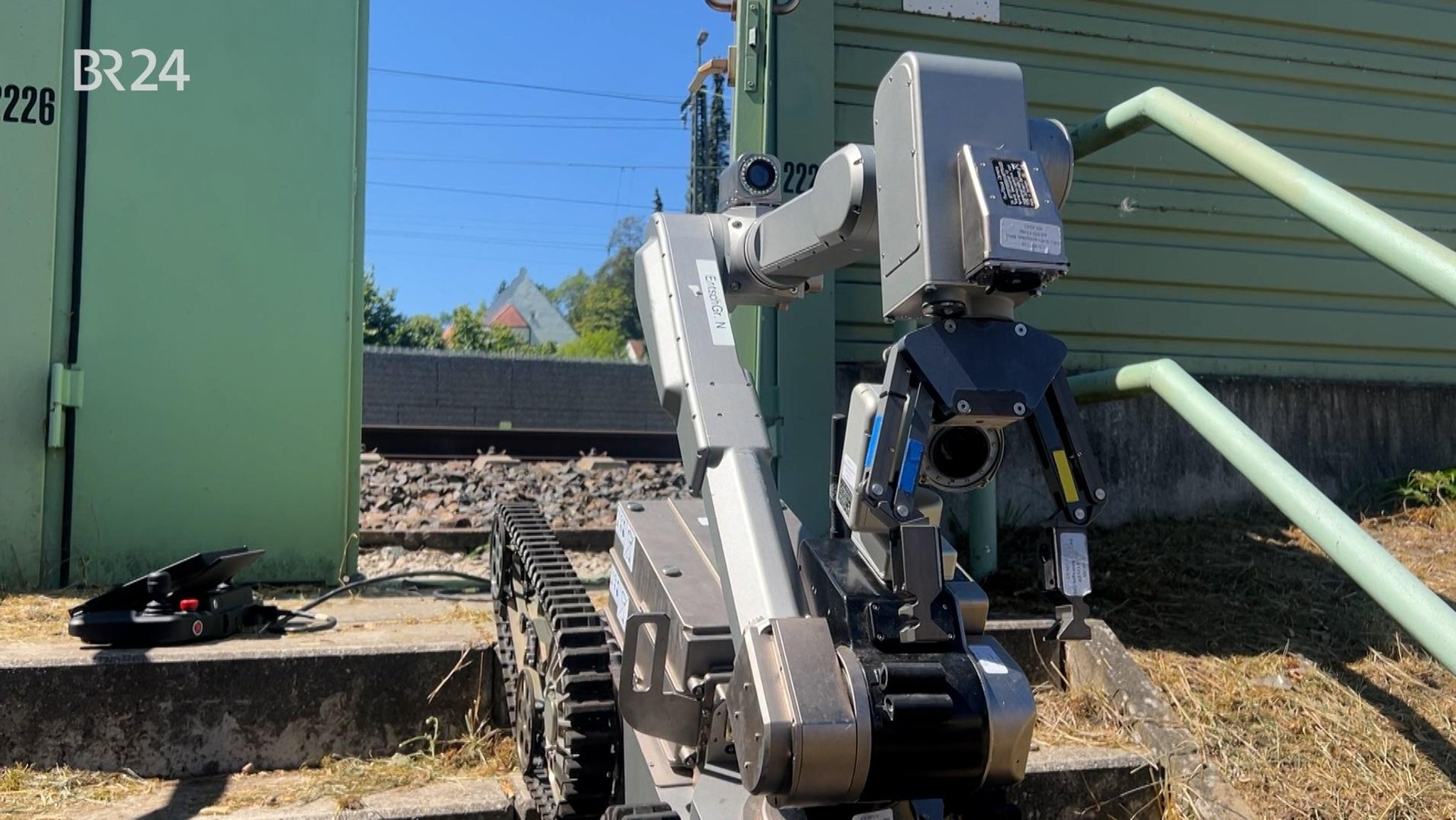 Ein Roboter auf Ketten in Nahaufnahme, dahinter eine grüne Lärmschutzwand und dahinter Bahngleise. Mit dem Roboter wurde der verdächtige Gegenstand untersucht. | Bild: Bayerischer Rundfunk 2026 Ein Roboter auf Ketten in Nahaufnahme, dahinter eine grüne Lärmschutzwand und dahinter Bahngleise. Mit dem Roboter wurde der verdächtige Gegenstand untersucht.