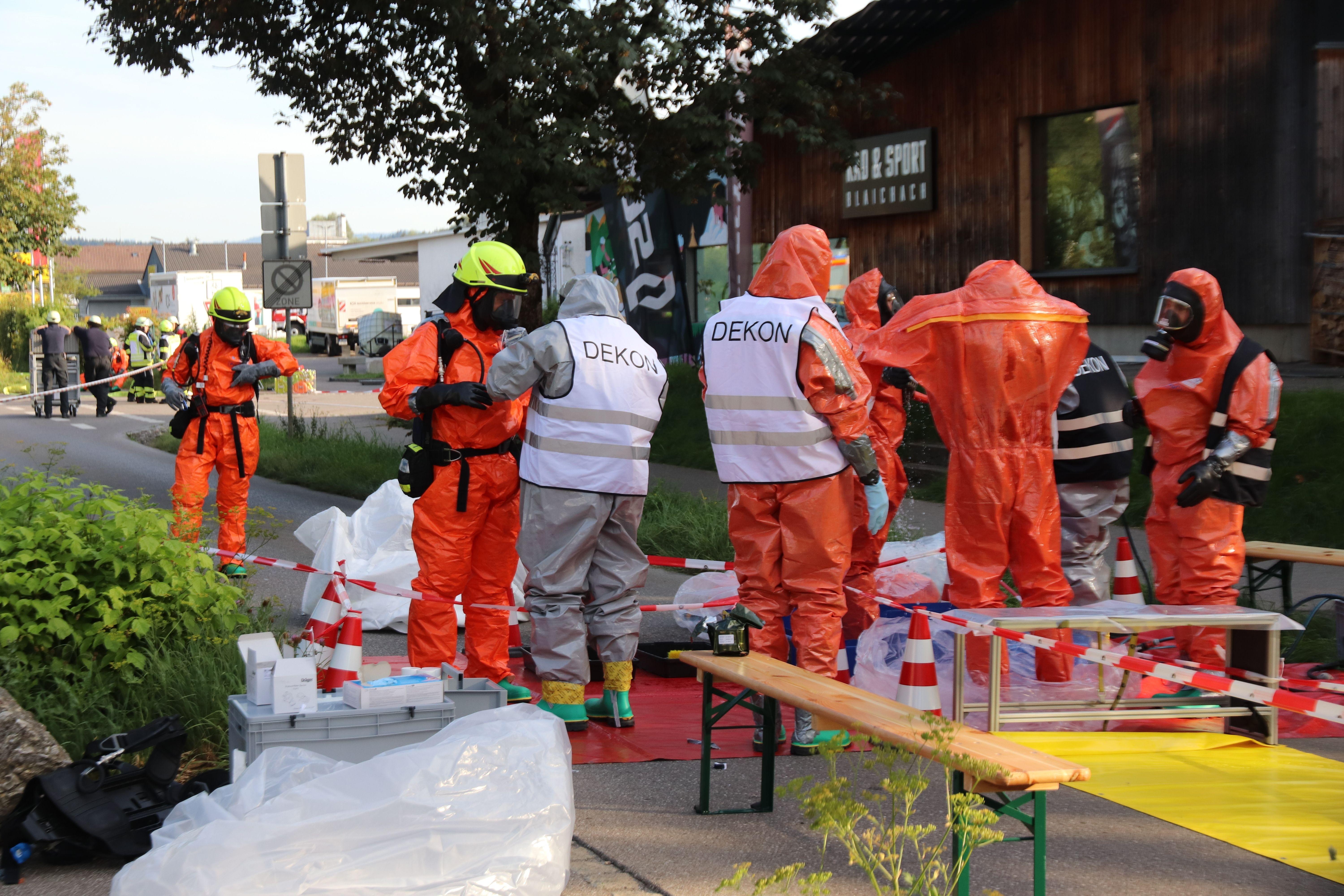Feuerwehrkräfte stehen in orangen Spezialanzügen und mit Atemmasken nach dem Chemieunfall in Blaichach auf der Straße.