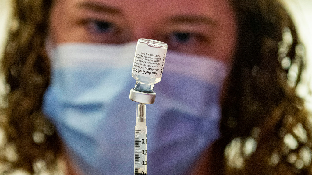 Eine Frau mit Maske zieht eine Spritze mit einem Corona-Impfstoff auf