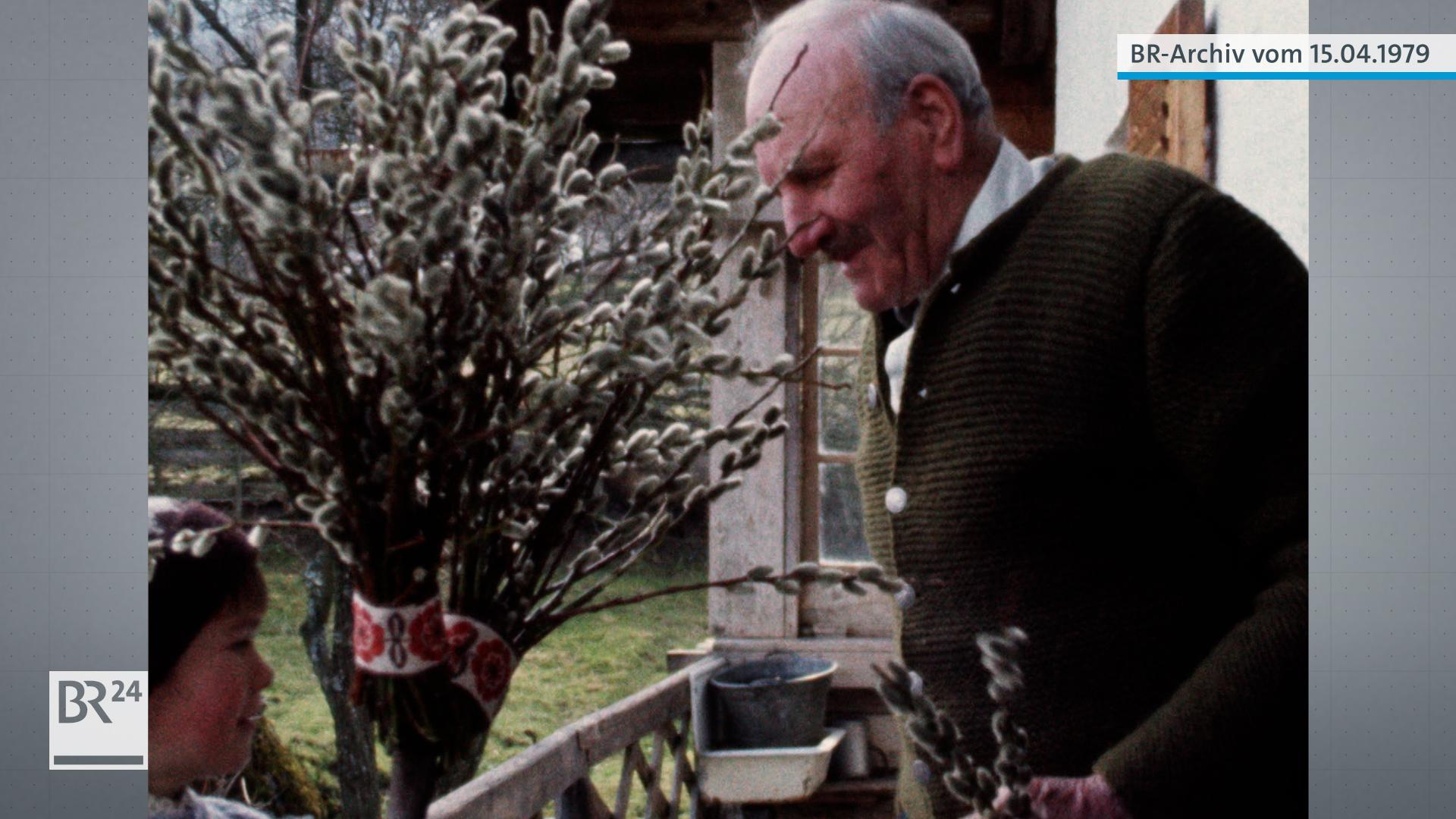Junge, links, hält einen Palmbuschen. Sein Großvater, rechts, hält zwei Palmzweige in der linken Hand