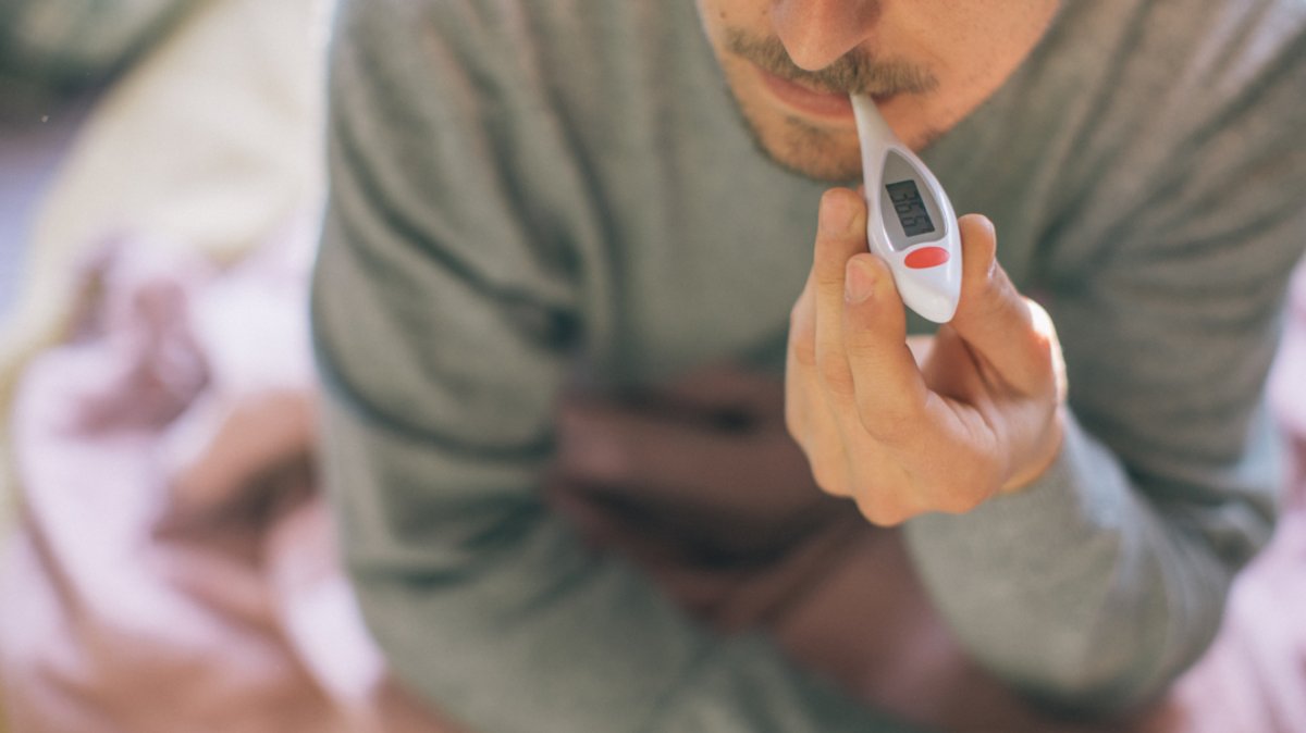 Ein Mann misst seine Temperatur mit einem Fieberthermometer (Symbolbild)