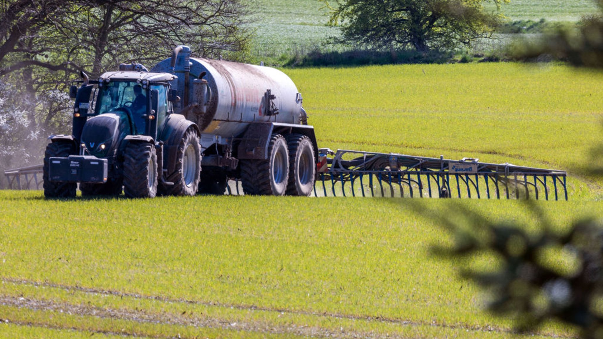 Archivbild: Ein Traktor zieht einen Tankwagen über ein Feld und verteilt Gülle im Boden. 