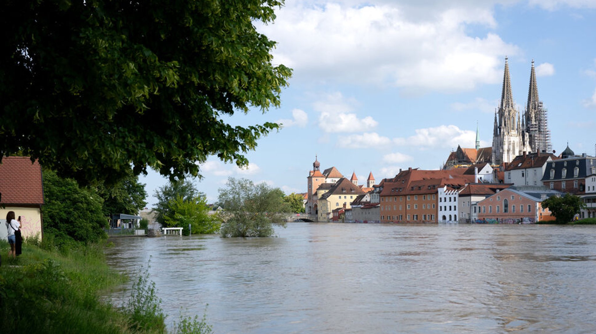 04.06.2024, Bayern, Regensburg: Ein Frau (l) fotografiert in der Altstadt am Donauufer das Hochwasser. Seit Tagen kämpfen die Helfer in Bayern gegen die Flut und ihre Folgen. Foto: Sven Hoppe/dpa +++ dpa-Bildfunk +++