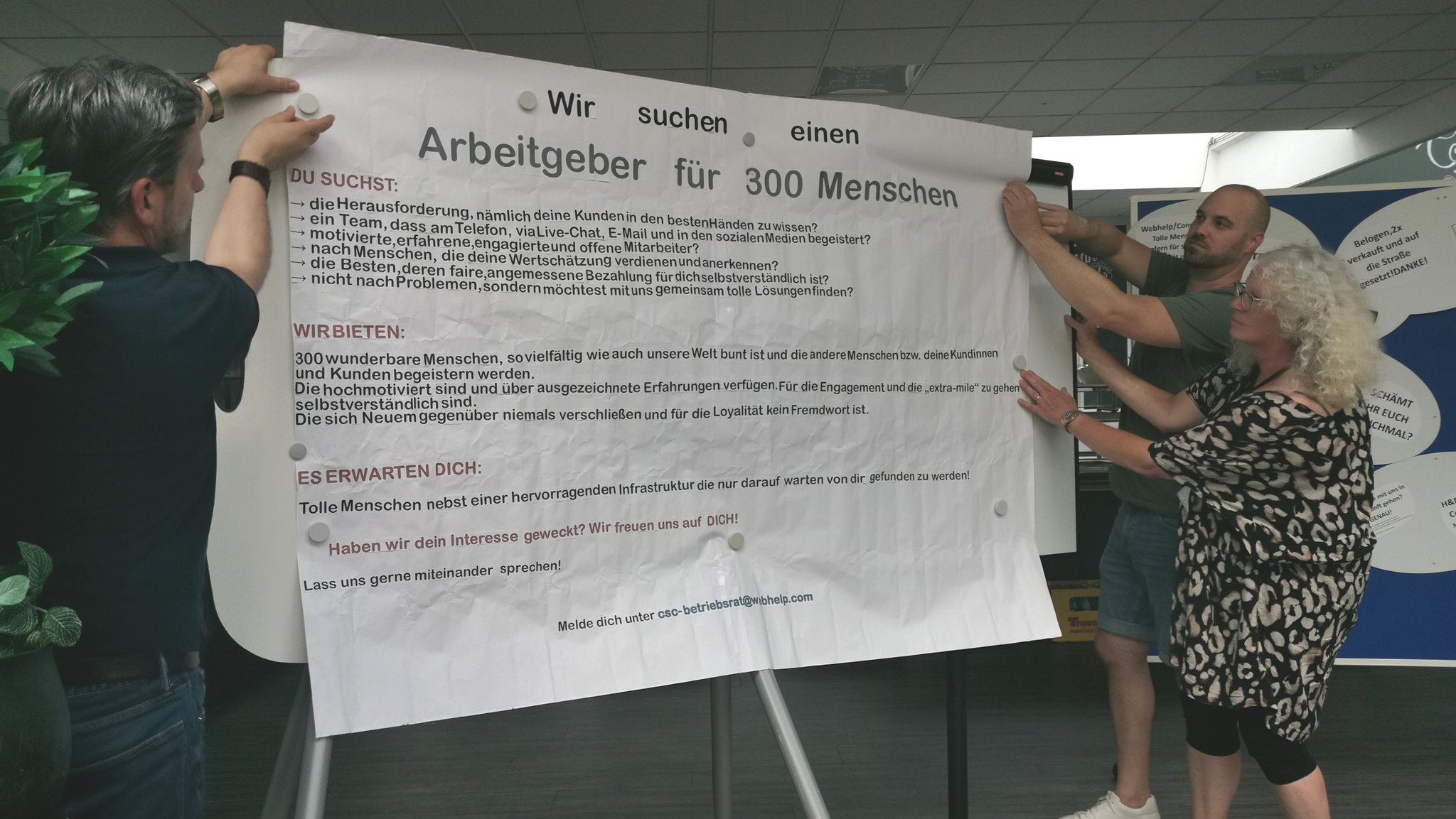 Menschen neben einem Plakat mit der Aufschrift: "Wir suchen einen Arbeitgeber für 300 Menschen"