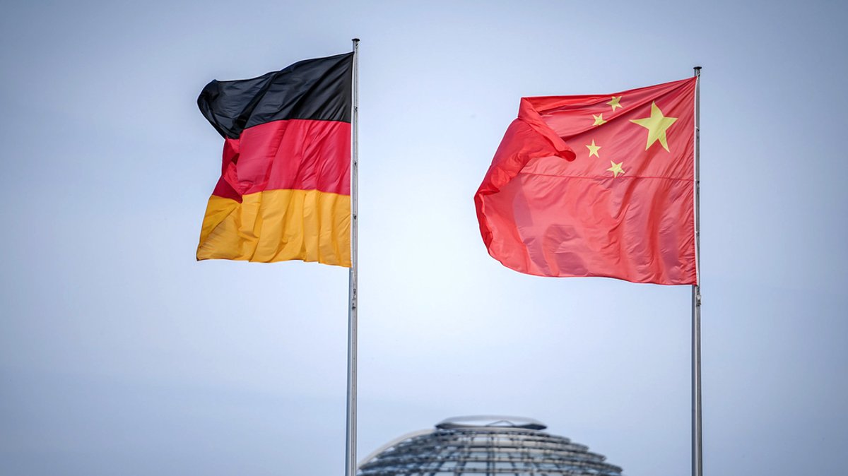 Die Flaggen von Deutschland und China wehen vor dem Bundeskanzleramt, im Hintergrund die Kuppel des Reichstagsgebäudes.