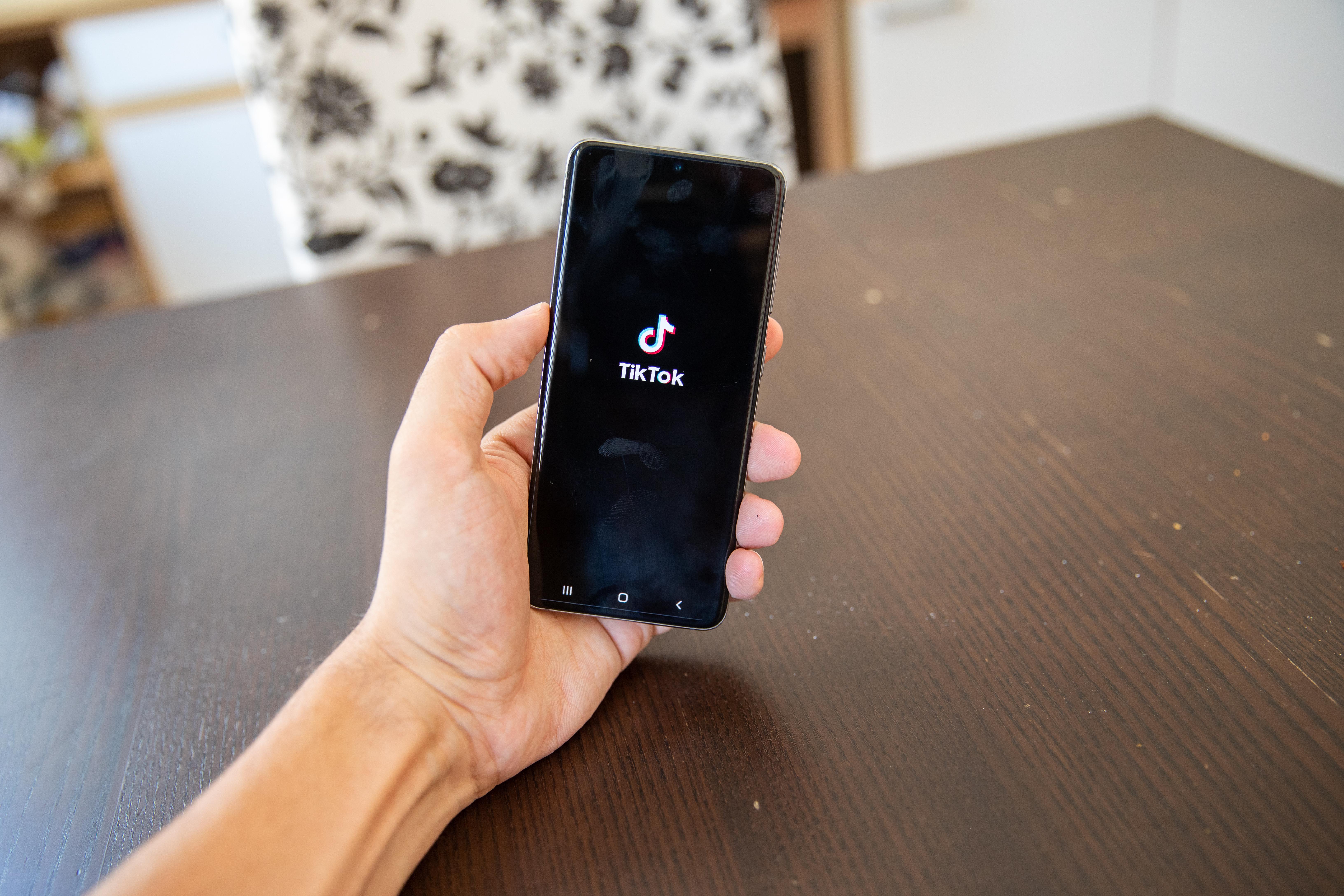 Eine Hand hält ein Smartphone, auf dem Bildschirm ist ein TikTok-Emblem zu sehen.