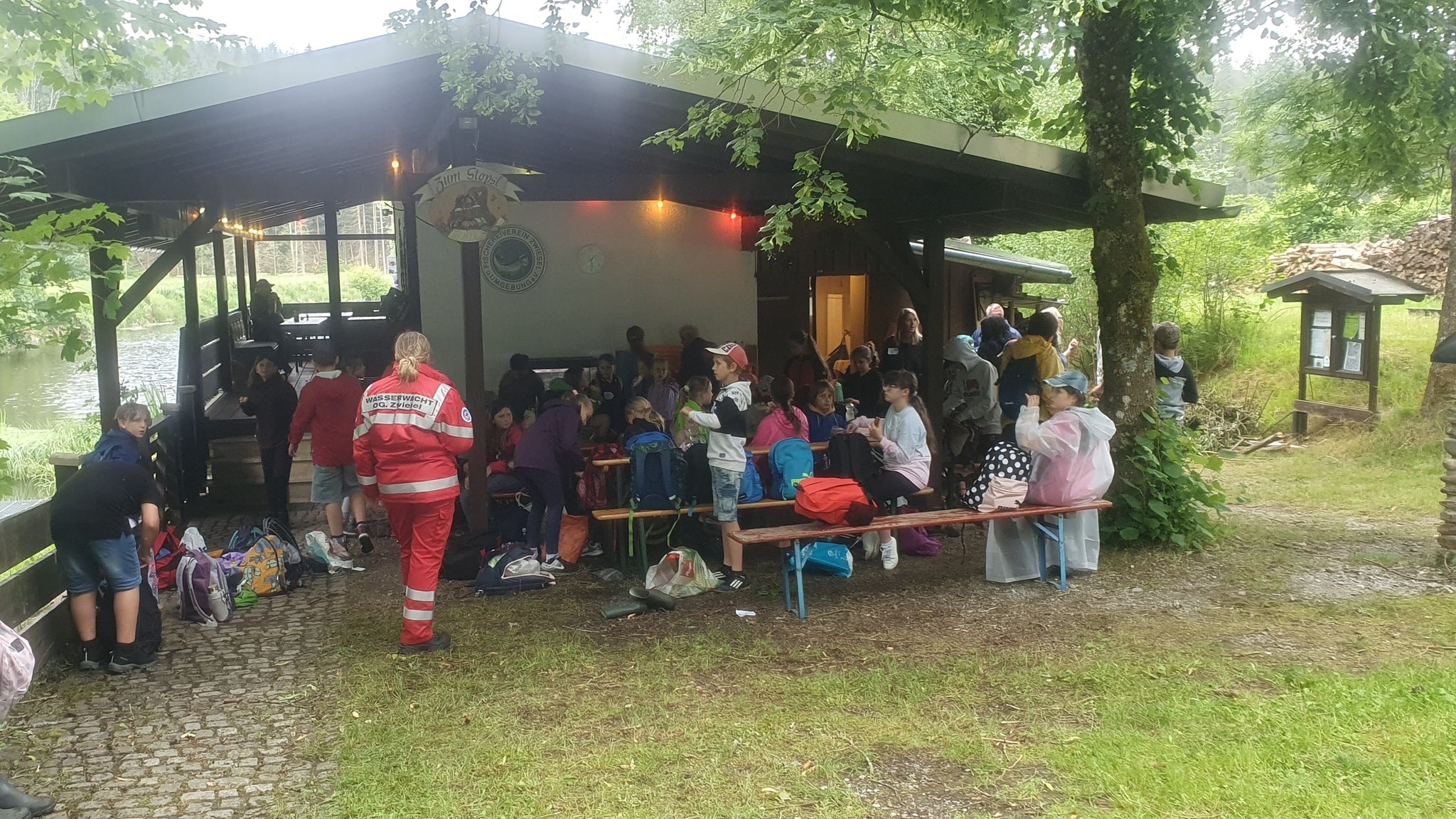 Deutsche und tschechische Kinder sitzen gemeinsam zur Brotzeit vor einer Hütte am Bach. 