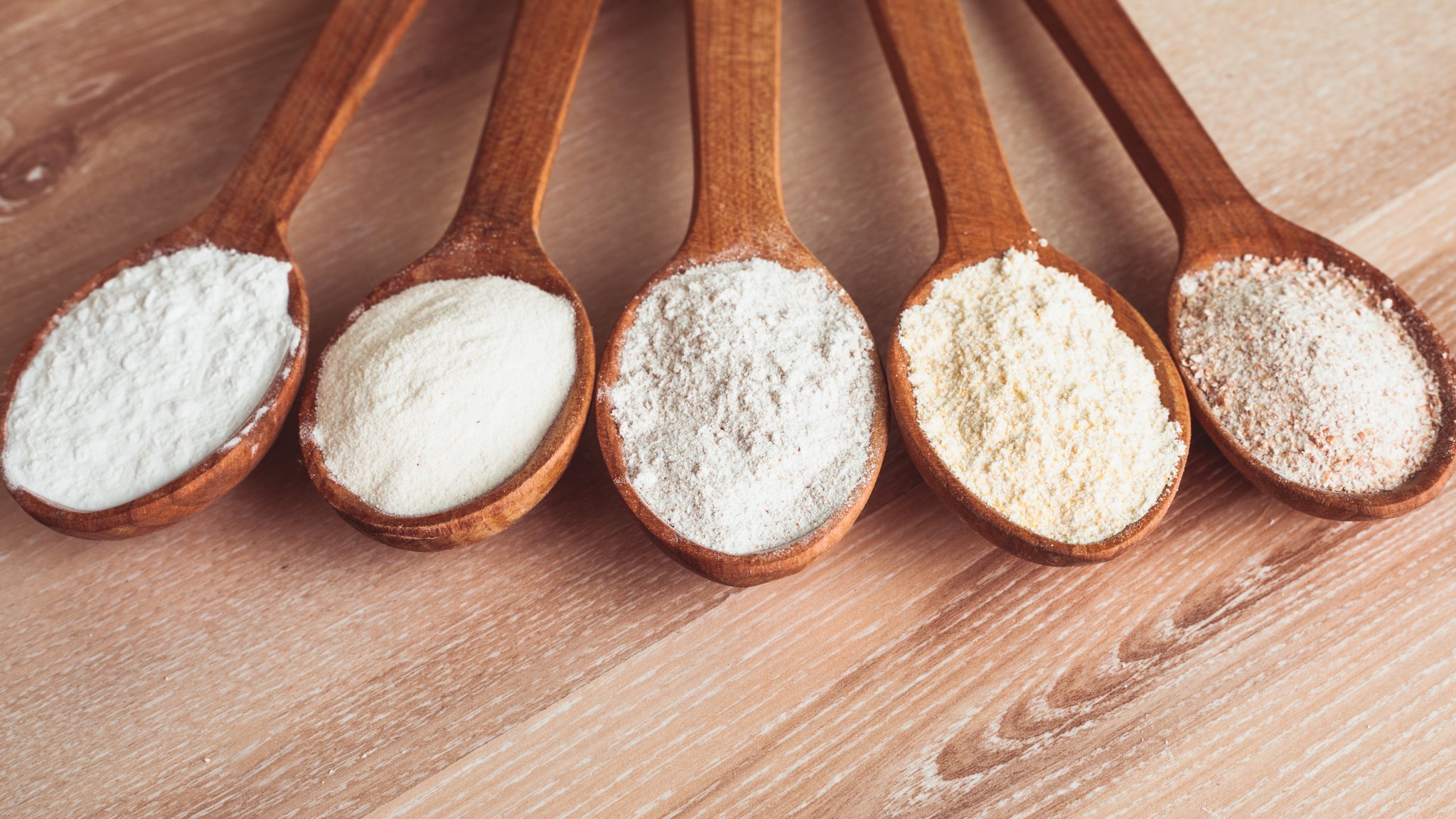 Verschiedene Holzlöffel nebeneinander mit verschiedenen Mehltypen 