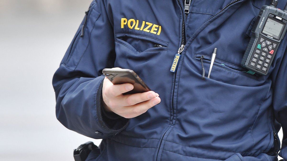 Ein bayerischer Polizist tippt etwas in ein Smartphone.