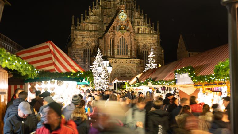 Nürnberger Christkindlesmarkt mit der beleuchteten Westfassade der Frauenkirche im Hintergrund.
| Bild:adobestock