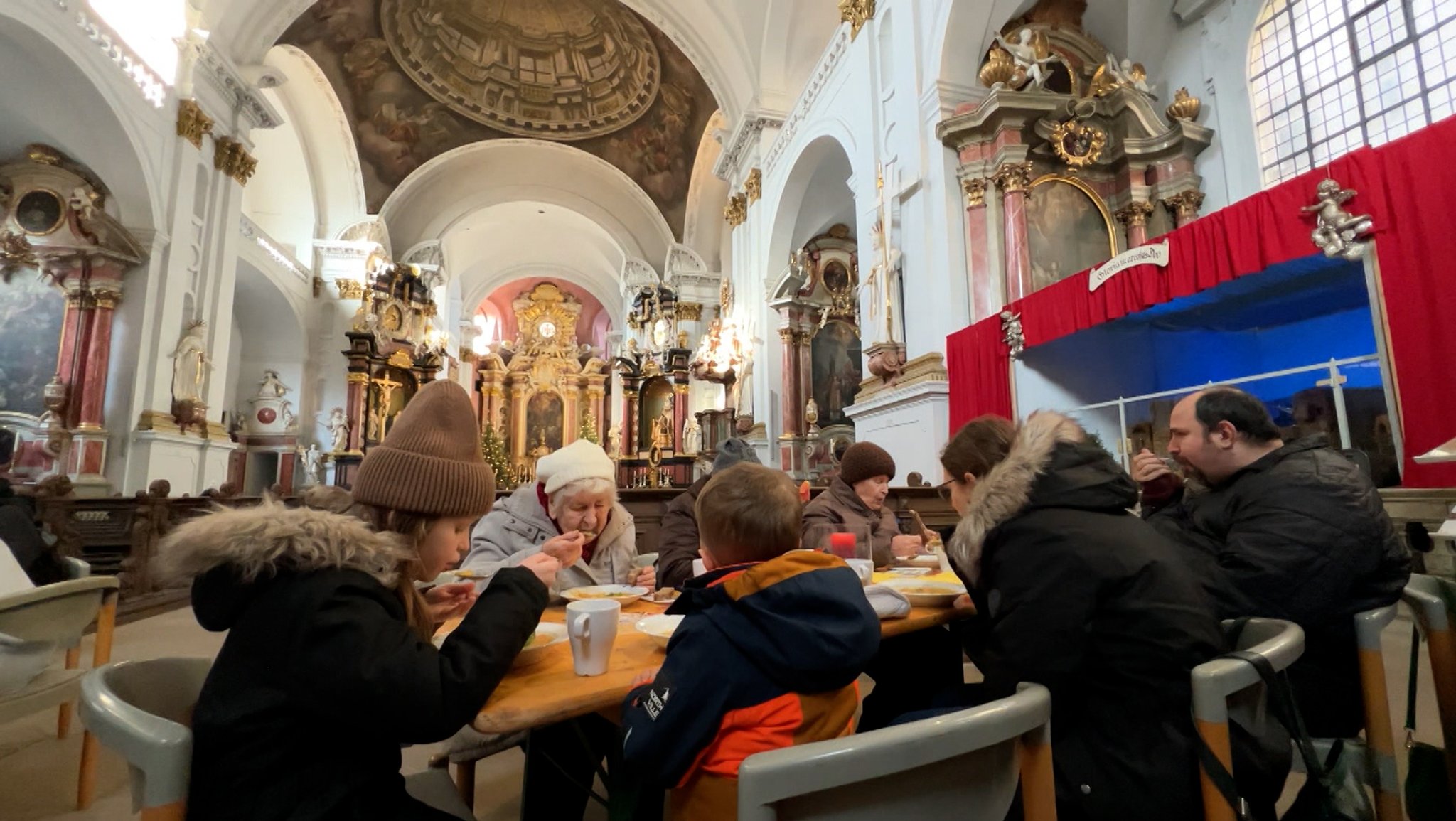 Menschen sitzen in einer Kirche am Tisch und essen Suppe.