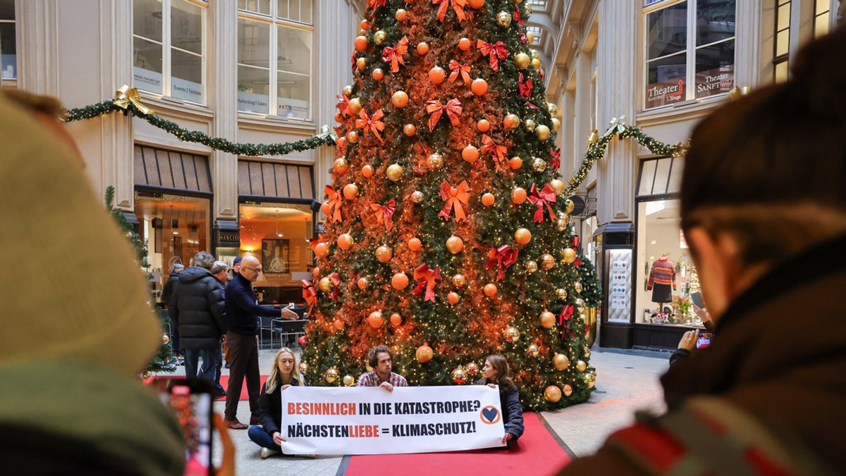 Mitglieder der Protestgruppe ·"Letzte Generation" sitzen vor einem mit Farbe besprühten Weihnachtsbaum in der Leipziger Mädler-Passage 