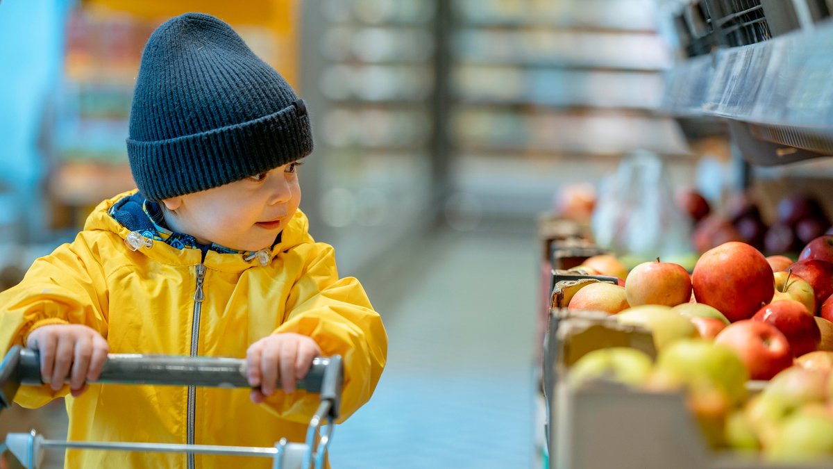 Viele Verbraucherinnen und Verbraucher sparen inzwischen bei Lebensmitteln - die verringerte Nachfrage drückt die Preise. Ein Kind steht vor einem Apfelregal und denkt offenbar darüber nach, einen mitzunehmen.