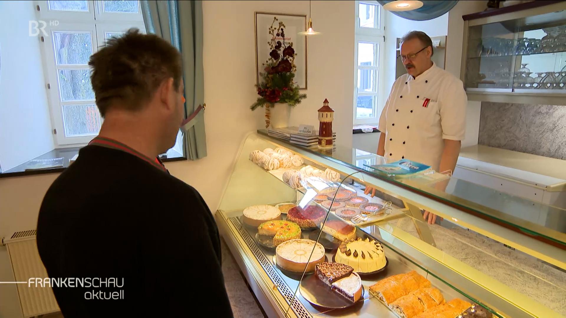 Ein Mann steht hinterm Kuchen-Tresen und bedient einen Kunden.