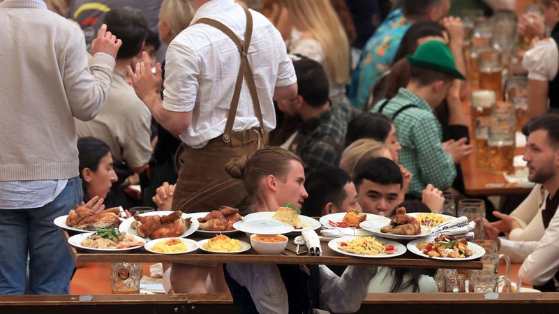 06.10.2024, Bayern, München: Eine Bedienung trägt im Paulaner-Festzelt Speisen auf einem Tablet. Die Wiesn findet vom 21. September bis 6. Oktober 2024 statt. Foto: Karl-Josef Hildenbrand/dpa +++ dpa-Bildfunk +++ | Bild: dpa-Bildfunk/Karl-Josef Hildenbrand 06.10.2024, Bayern, München: Eine Bedienung trägt im Paulaner-Festzelt Speisen auf einem Tablet. Die Wiesn findet vom 21. September bis 6. Oktober 2024 statt. Foto: Karl-Josef Hildenbrand/dpa +++ dpa-Bildfunk +++