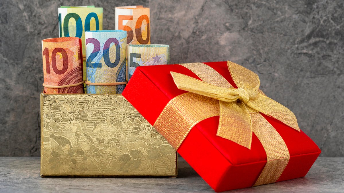Ein verpacktes Geschenk, dahinter ein Goldenes Kästchen aus dem Geldscheine herausschauen | Bild: picture alliance/Zoonar/Grazvydas Januska Ein verpacktes Geschenk, dahinter ein Goldenes Kästchen aus dem Geldscheine herausschauen