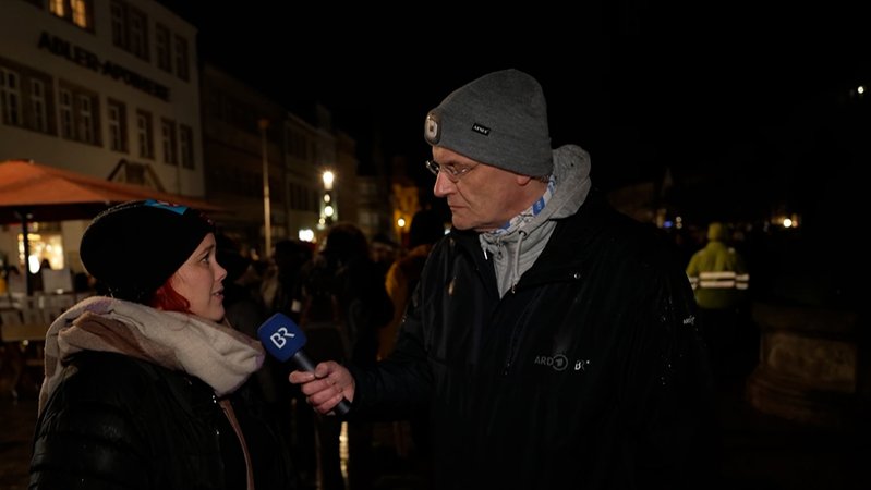Ein Reporter des BR interviewt in der Dunkelheit eine Frau. 