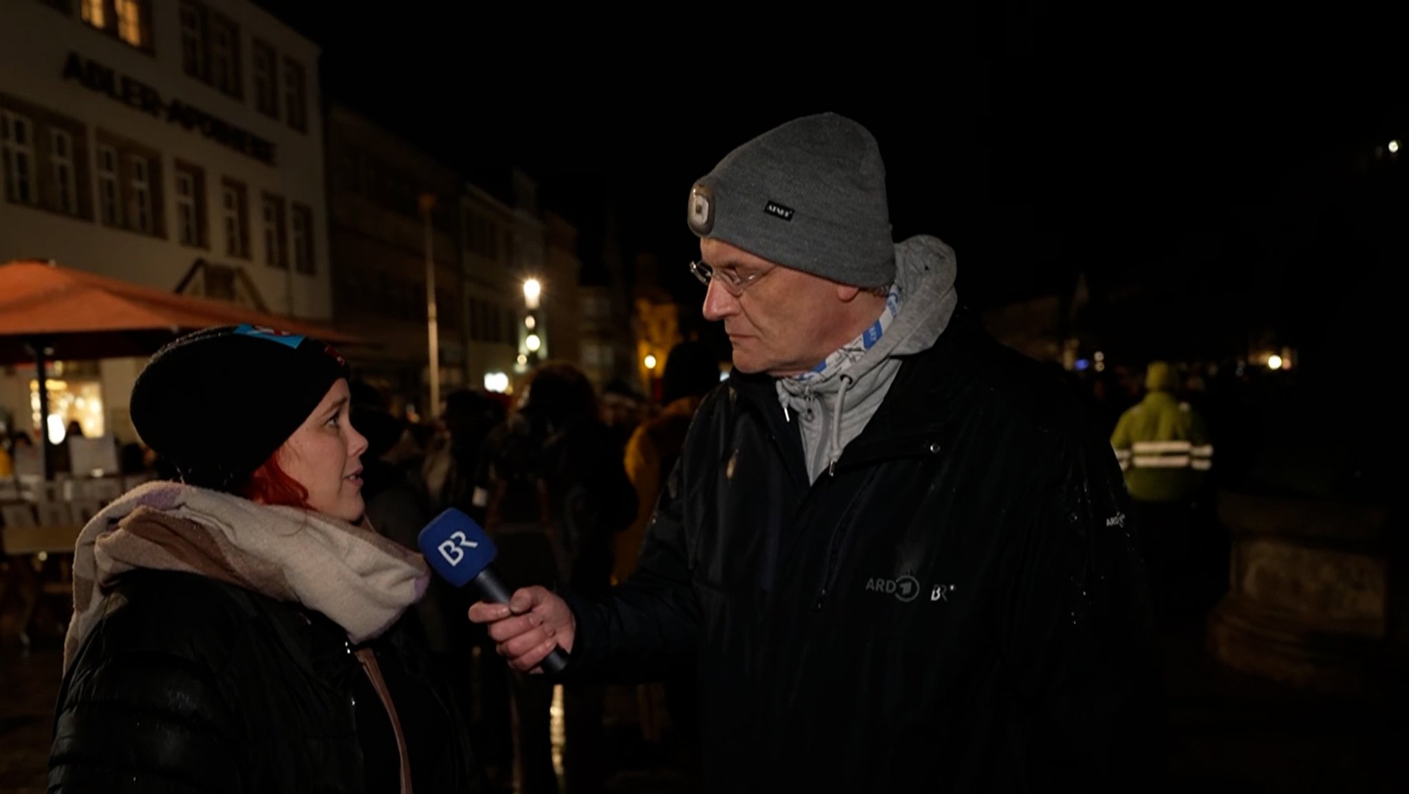 Ein Reporter des BR interviewt in der Dunkelheit eine Frau. 