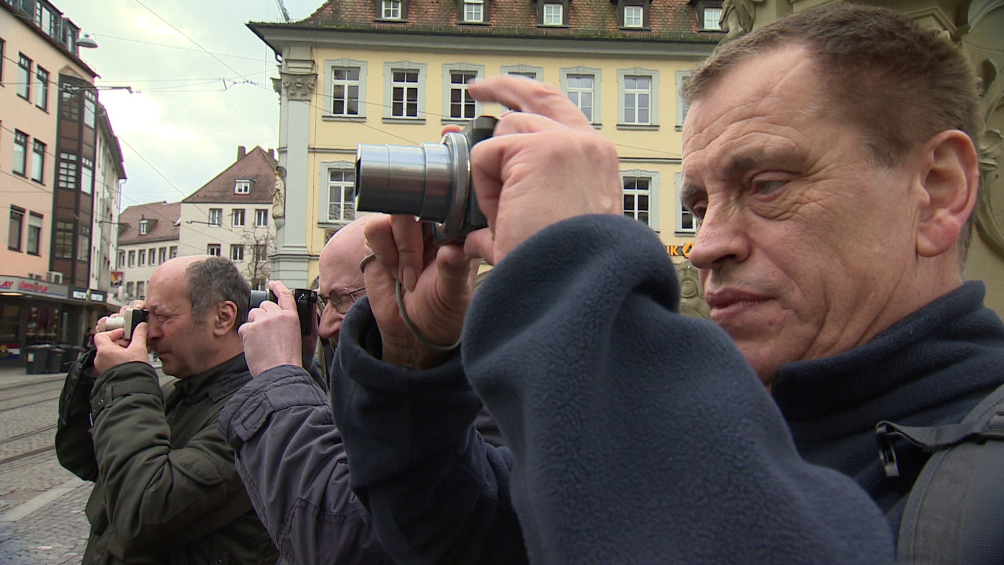 Drei Männer stehen nebeneinander und fotografieren etwas