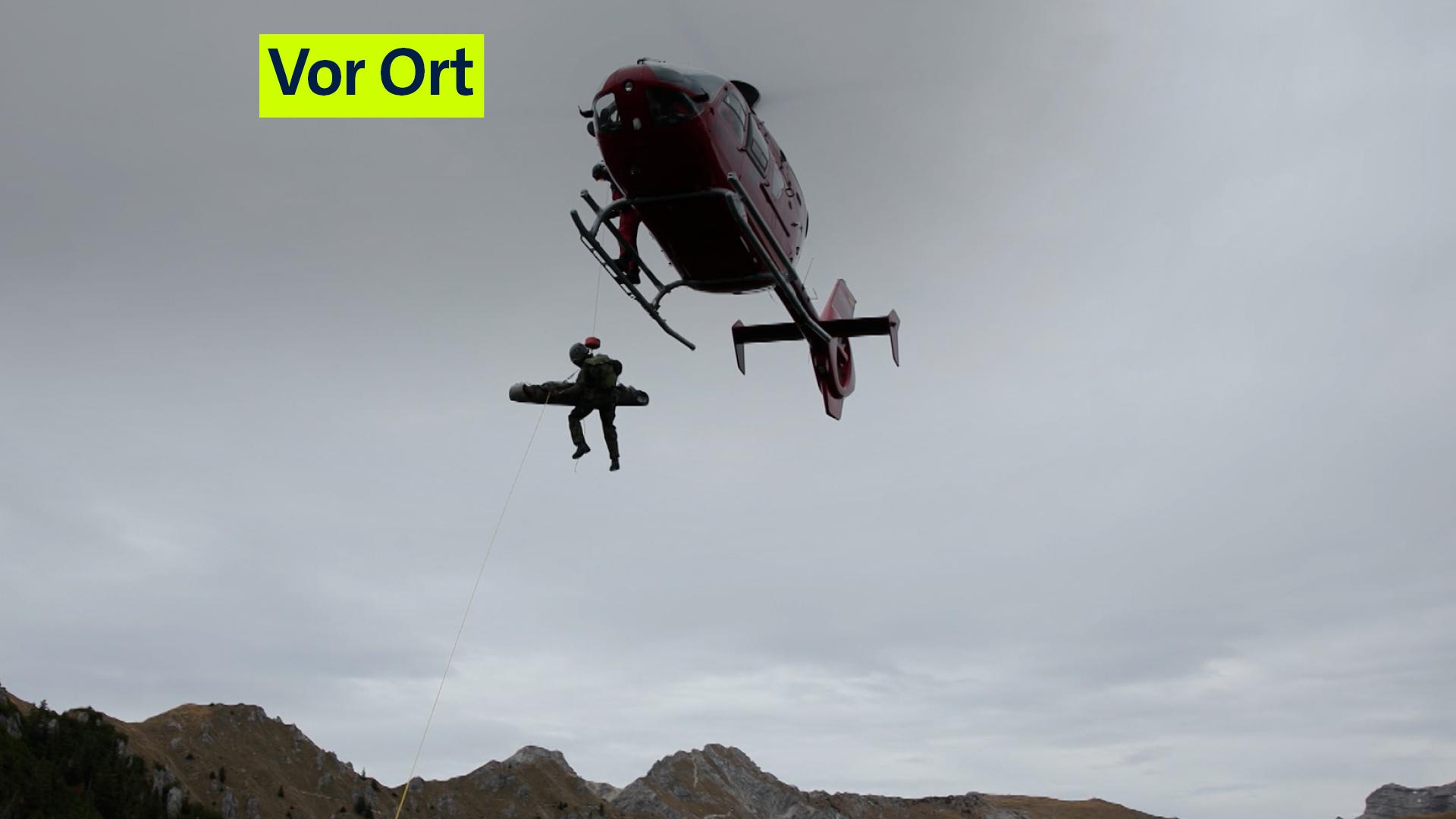 Zu sehen ist ein Helikopter, der per Seilwinde einen Soldaten und eine Trage emporhebt.