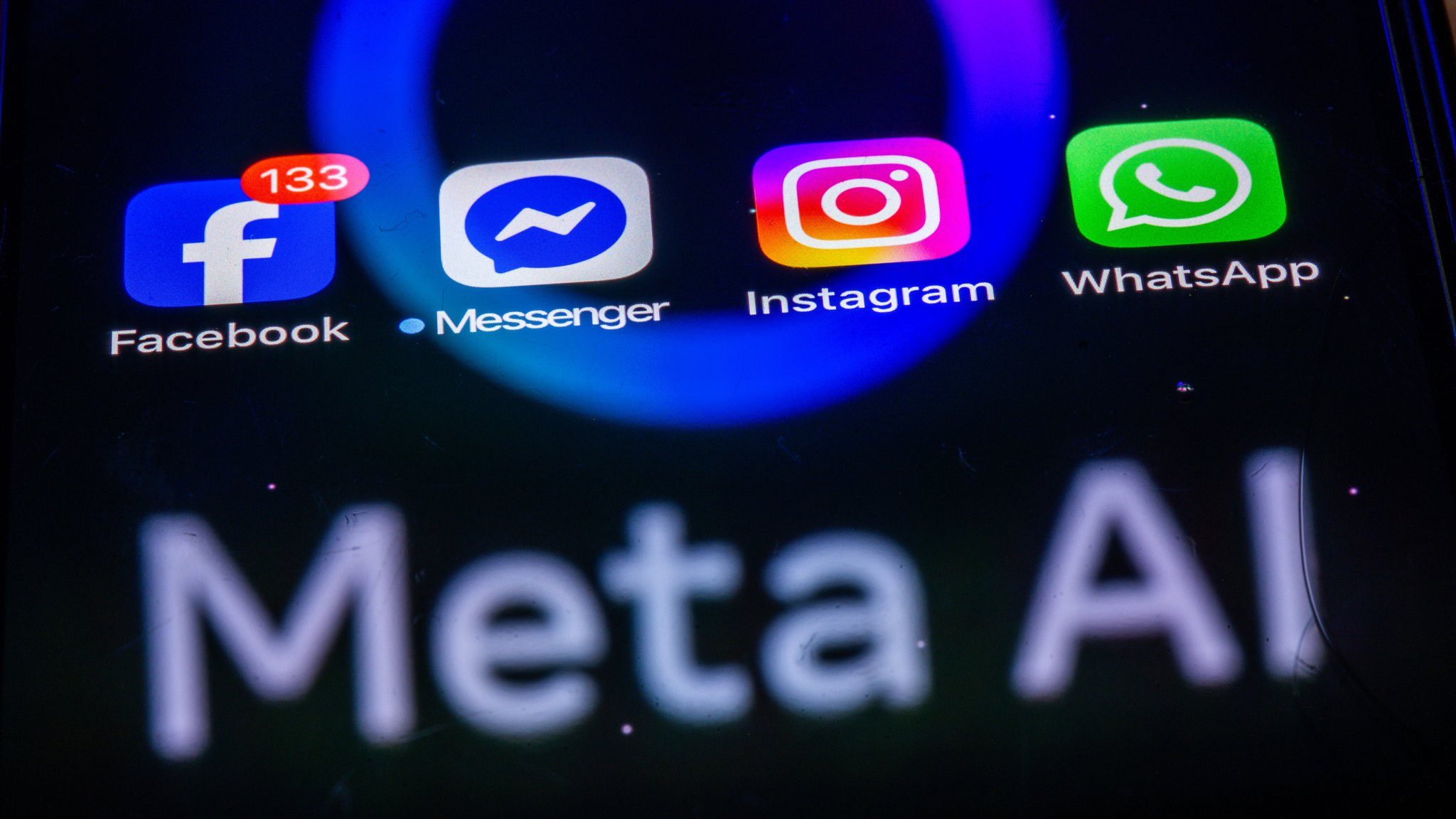 (Symbolbild) Die Apps Facebook, Messenger, Instagram und WhatsApp werden auf einem Smartphone-Display angezeigt in dem das Logo der KI-Anwendung Meta AI spiegelt.