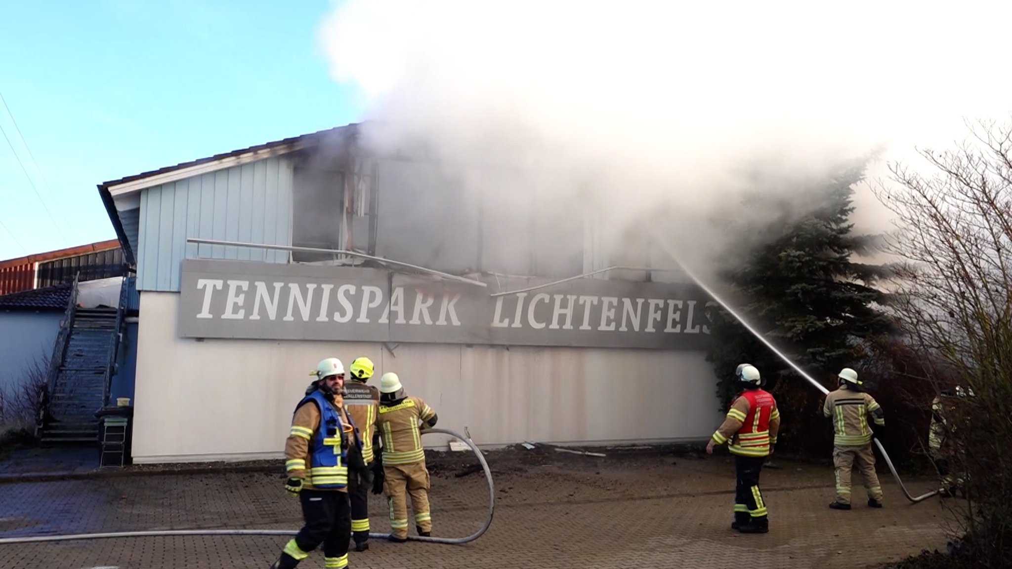 Feuerwehrkräfte stehen vor dem brennenden Tennispark Lichtenfels.