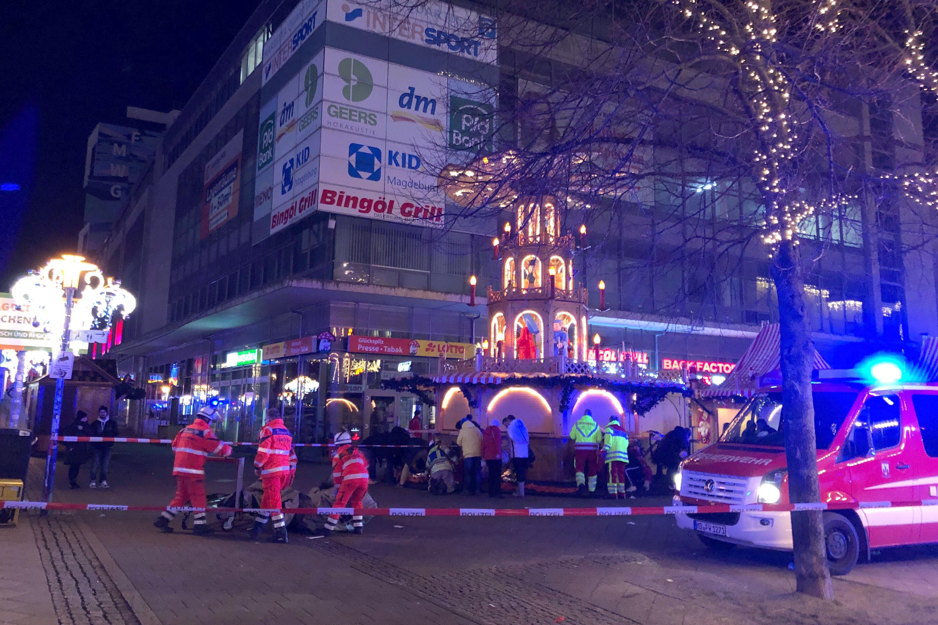 Rettungskräfte in orangener und rot-neongelber Montur sind auf einem abgesperrten Platz beschäftigt. Im rechten Vordergrund ein Feuerwehrfahrzeug, im Hintergrund eine mehrstöckige Weihnachtspyramide. In Magdeburg ist ein Autofahrer in eine Menschengruppe auf dem Weihnachtsmarkt gefahren. 
