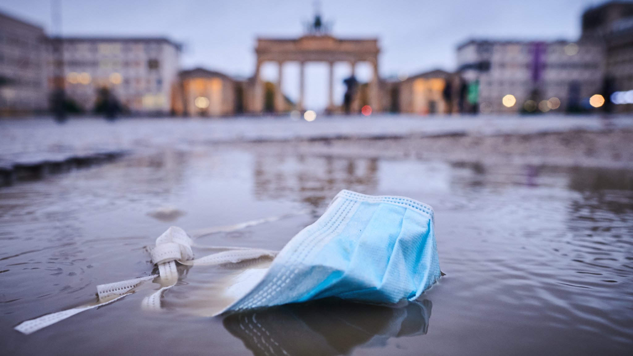 Eine Maske liegt in einer Regenpfütze vor dem Brandenburger Tor.