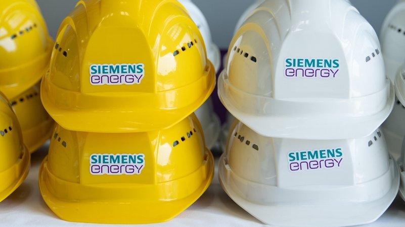 Schutzhelme mit der Aufschrift "Siemens Energy" liegen in einer Halle auf einem Tisch.