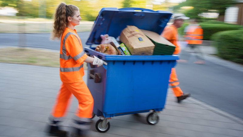 Eine Studentin in Warnkleidung schiebt eine Mülltonne. | Bild: picture alliance/dpa | Nicolas Armer Eine Studentin in Warnkleidung schiebt eine Mülltonne.