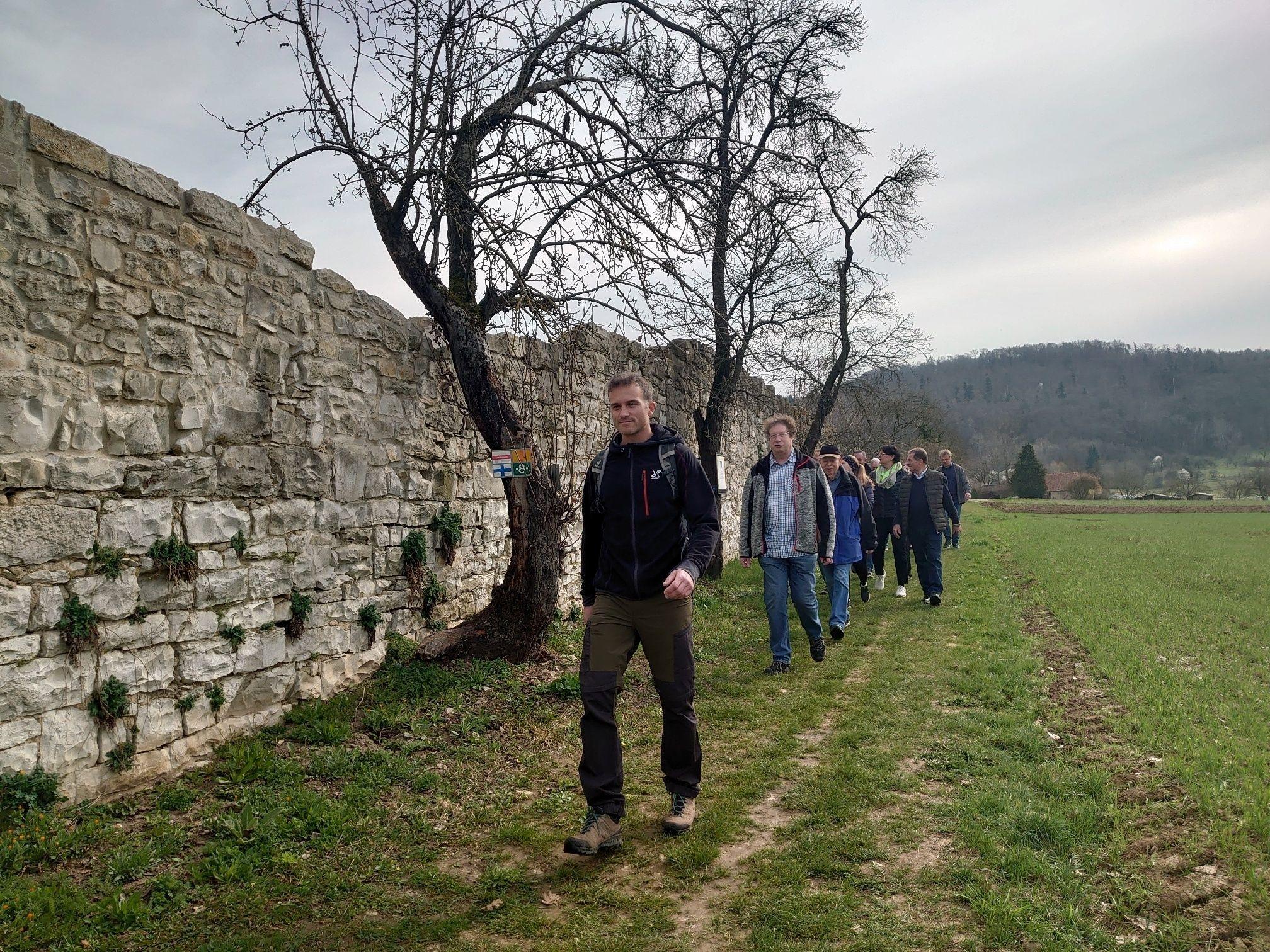 Eine Gruppe Wandernde gehen an der alten Klostermauer in Engelthal vorbei.