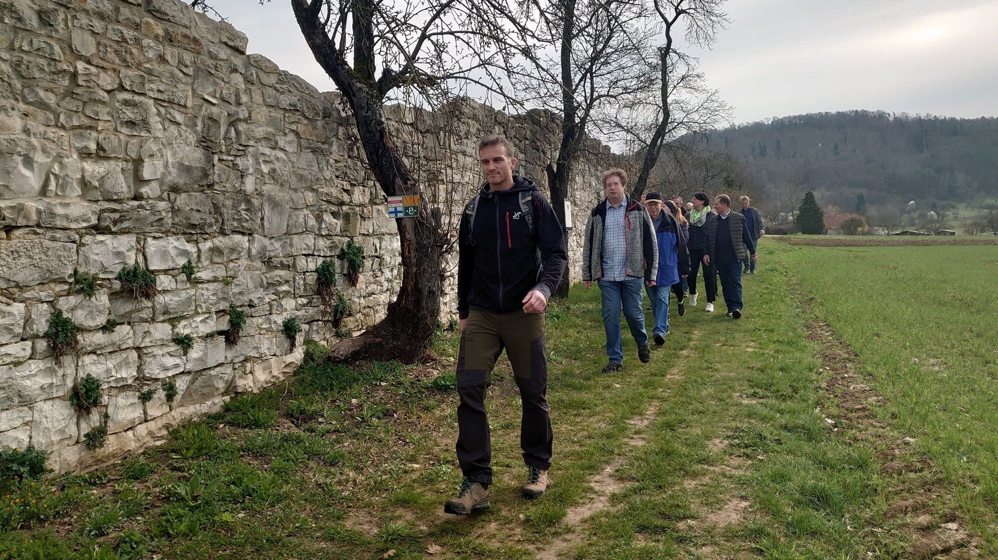 Eine Gruppe Wandernde gehen an der alten Klostermauer in Engelthal vorbei.