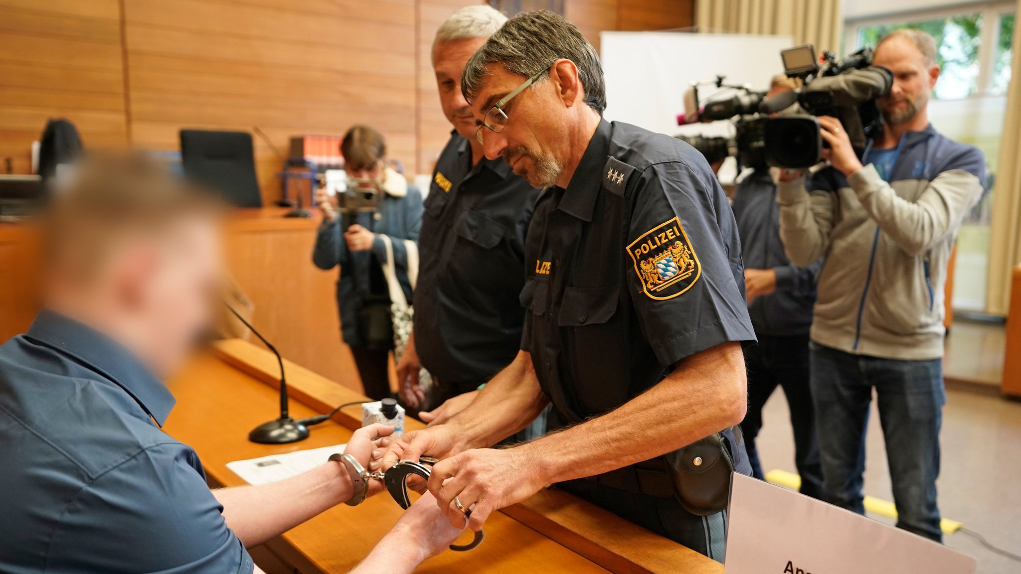 Archiv, 12.10.23: Justizbeamte nehmen dem Angeklagten im Landgericht Traunstein vor Prozessbeginn die Handschellen ab.