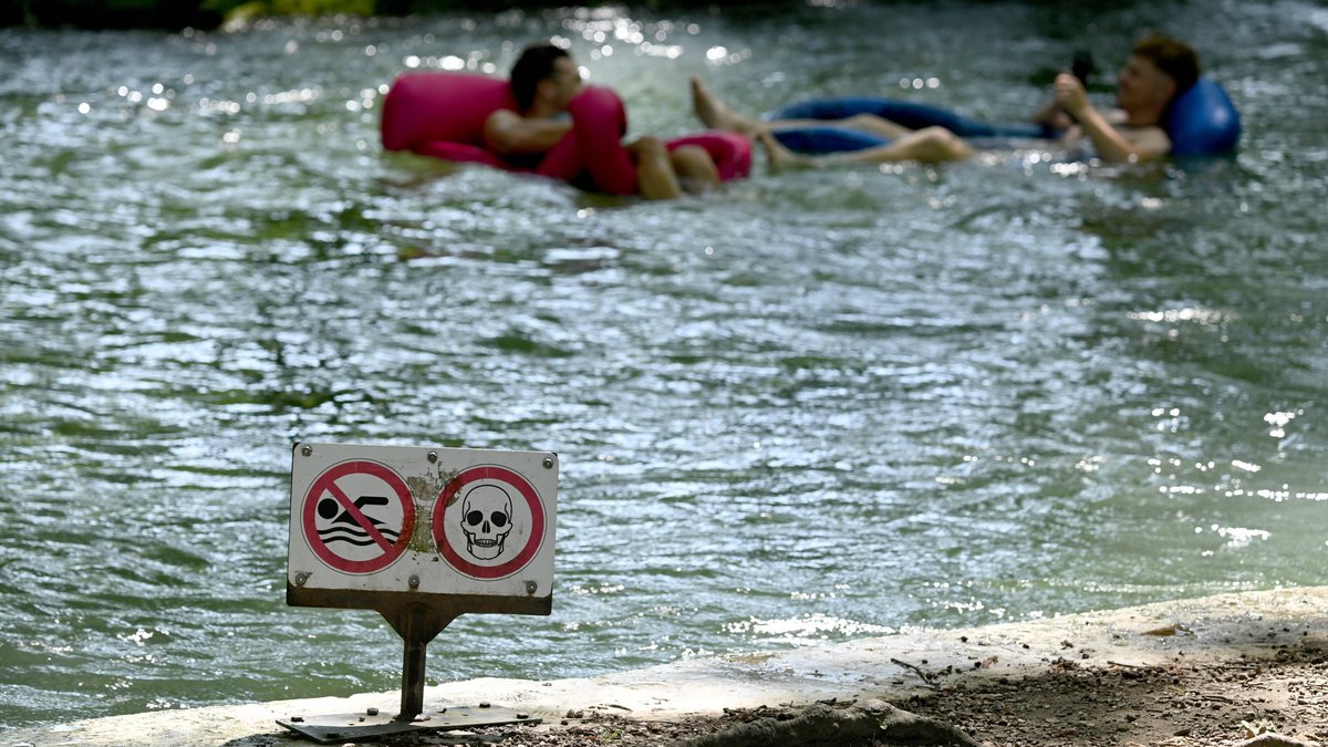 Zu sehen sind zwei junge Männern auf Luftmatratzen im Eisbach.