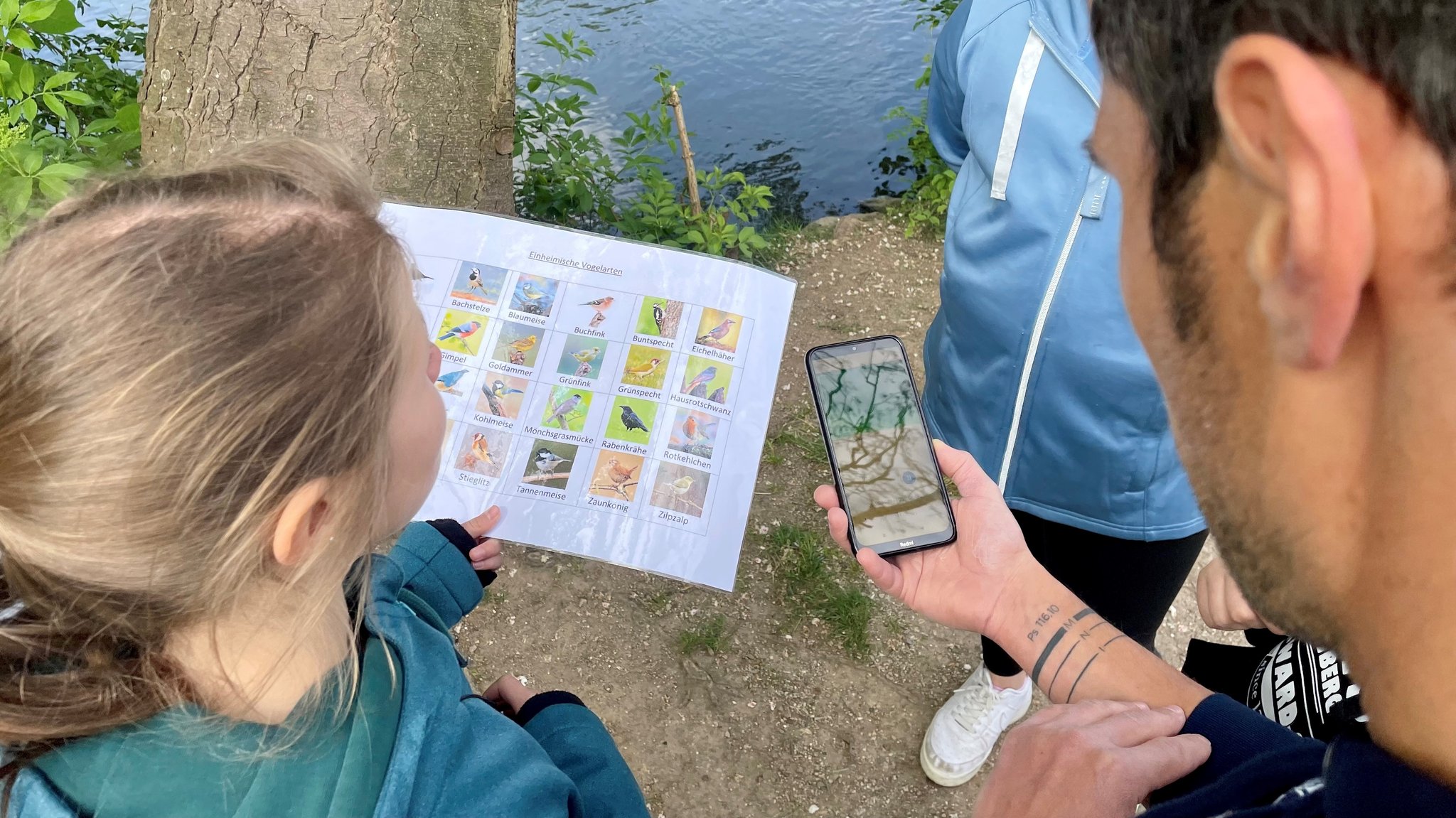 Ein Lehrer hält ein Smartphone in der Hand und steht neben einer Schülerin.