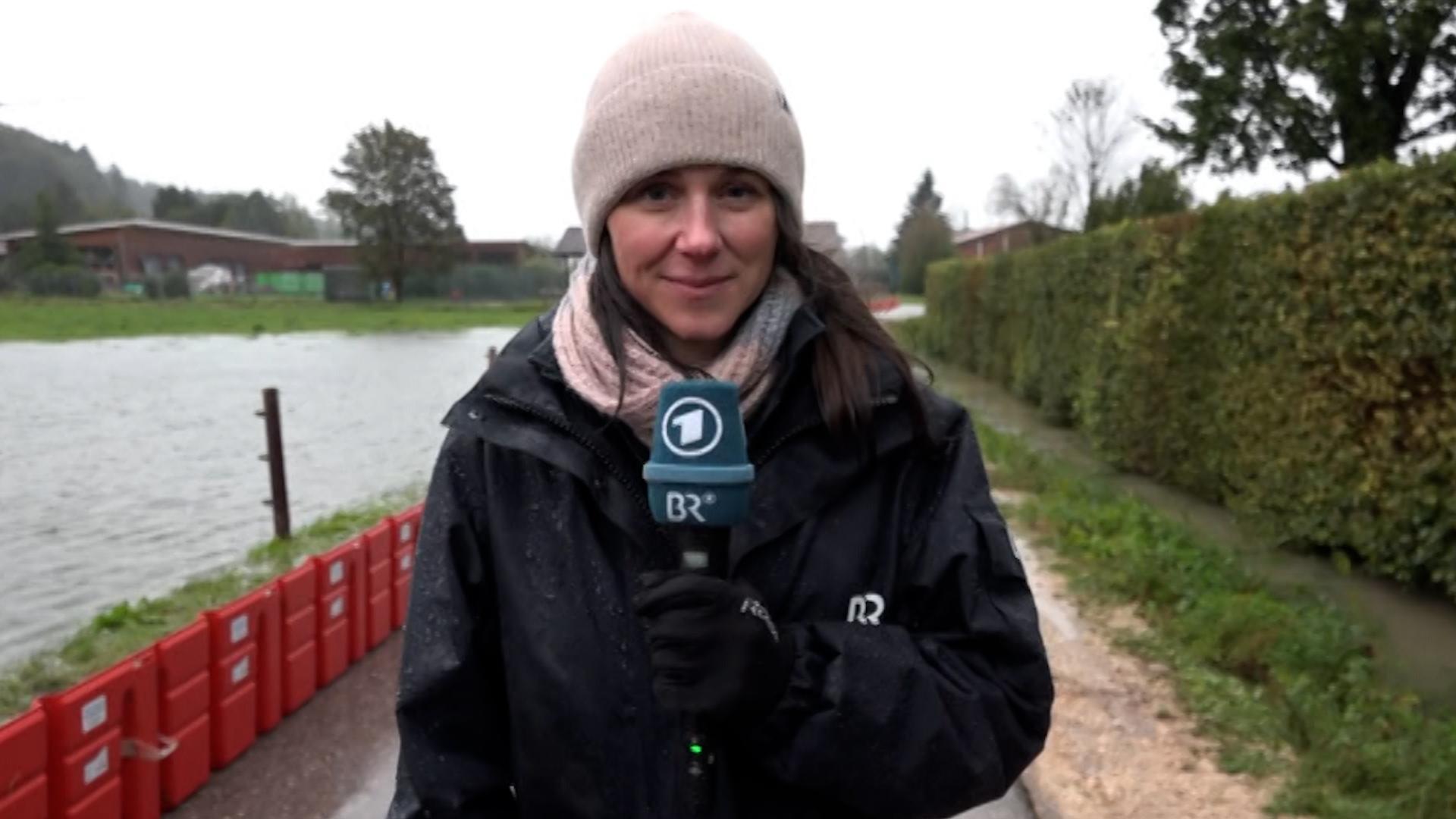 BR-Korrespondentin Theresa Momsen berichtet über die aktuelle Hochwasserlage im Berchtesgadener Land. Sie steht zwischen einem Hochwasser führenden Fluss und einer Hecke.
