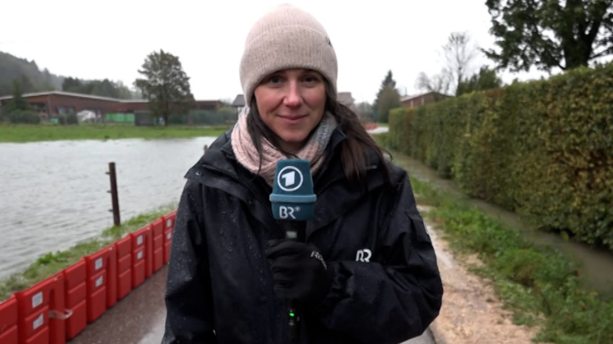 BR-Korrespondentin Theresa Momsen berichtet über die aktuelle Hochwasserlage im Berchtesgadener Land. Sie steht zwischen einem Hochwasser führenden Fluss und einer Hecke.