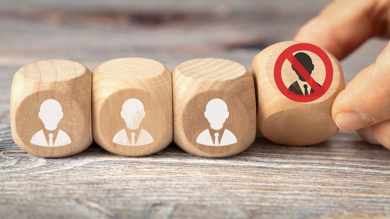 Holzwürfel mit Symbolen von Personen, einer wird entfernt und ist mit einem roten Kreis durchgestrichen. Symbolbild Stellenabbau. | Bild: picture alliance / CHROMORANGE / Michael Bihlmayer Holzwürfel mit Symbolen von Personen, einer wird entfernt und ist mit einem roten Kreis durchgestrichen. Symbolbild Stellenabbau.