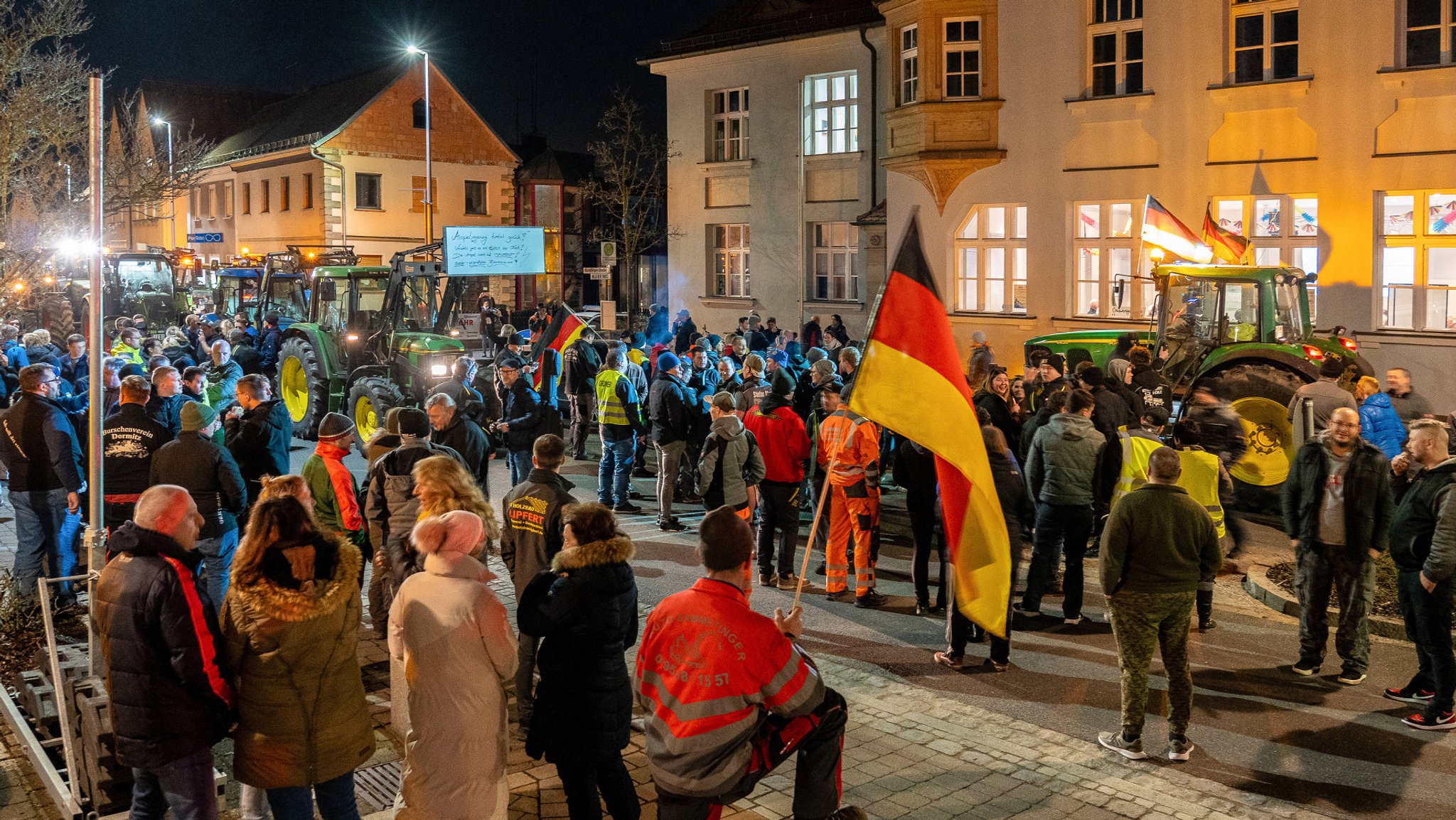 Viele Demonstranten, einige mit Deutschland-Fahnen, sind auf einem Platz, auf dem auch Traktoren parken. 