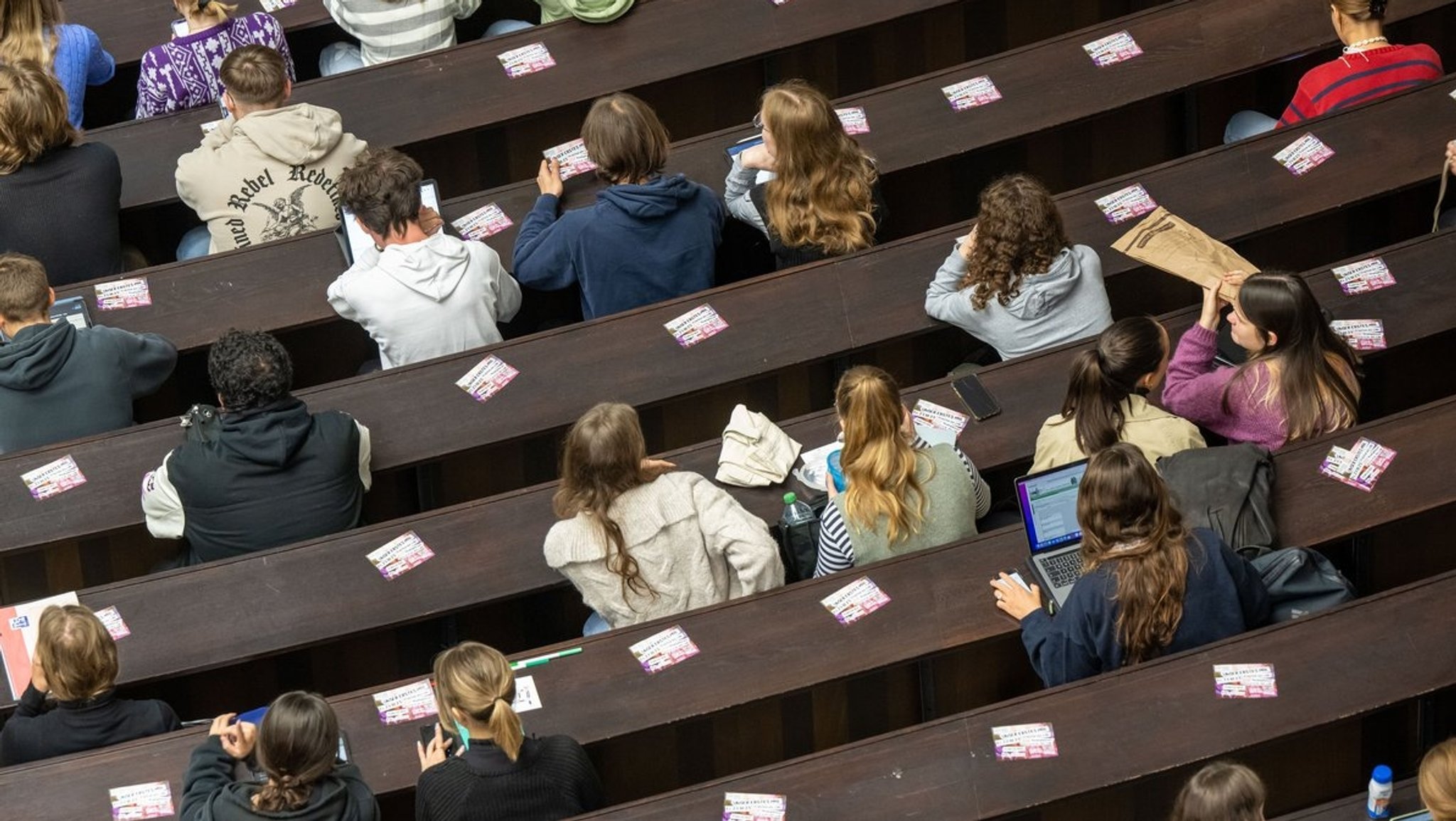 Blick von oben auf einen Hörsaal, in dem Studenten in Holzbänken sitzen. 