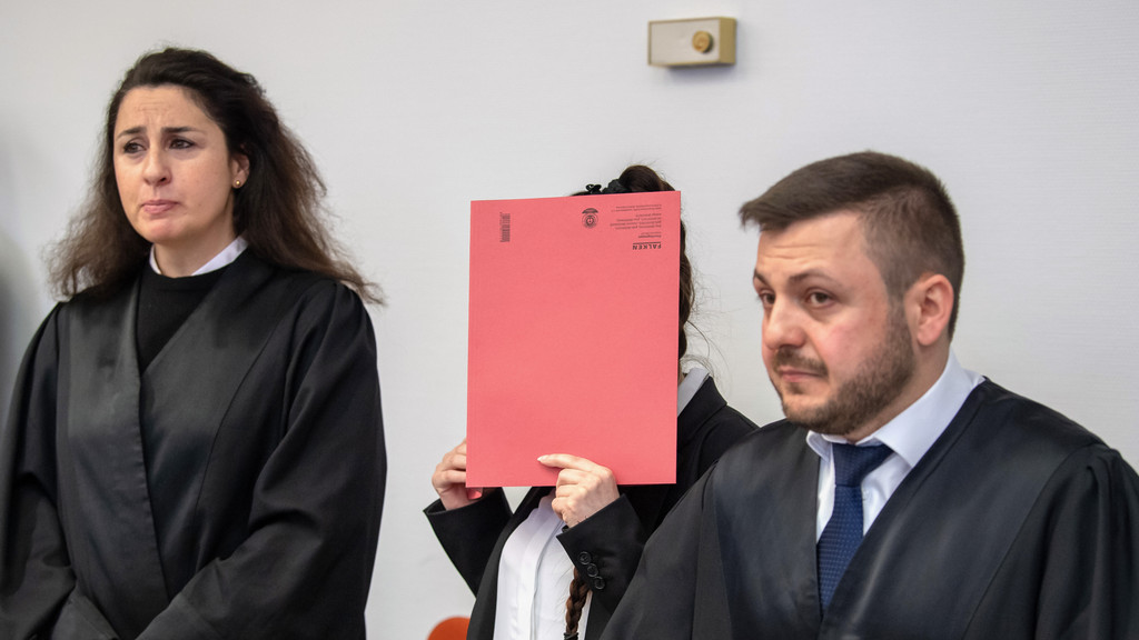 Archivbild: Die Angeklagte steht mit einem roten Aktendeckel vor ihrem Gesicht zu Prozessbeginn zwischen den Anwälten Sera Basay-Yildiz (l) und Ali Aydin (r) im Gerichtssaals.