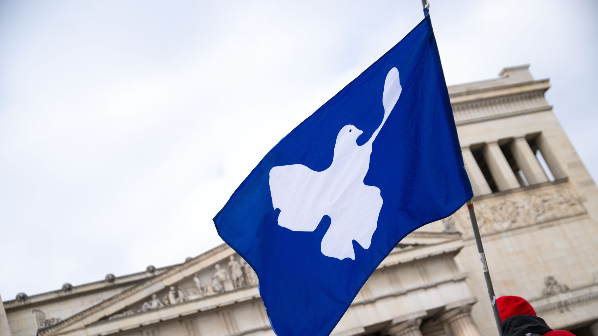 Symbolbild: Eine Fahne mit einer Friedenstaube weht am Münchner Königsplatz im Wind. 