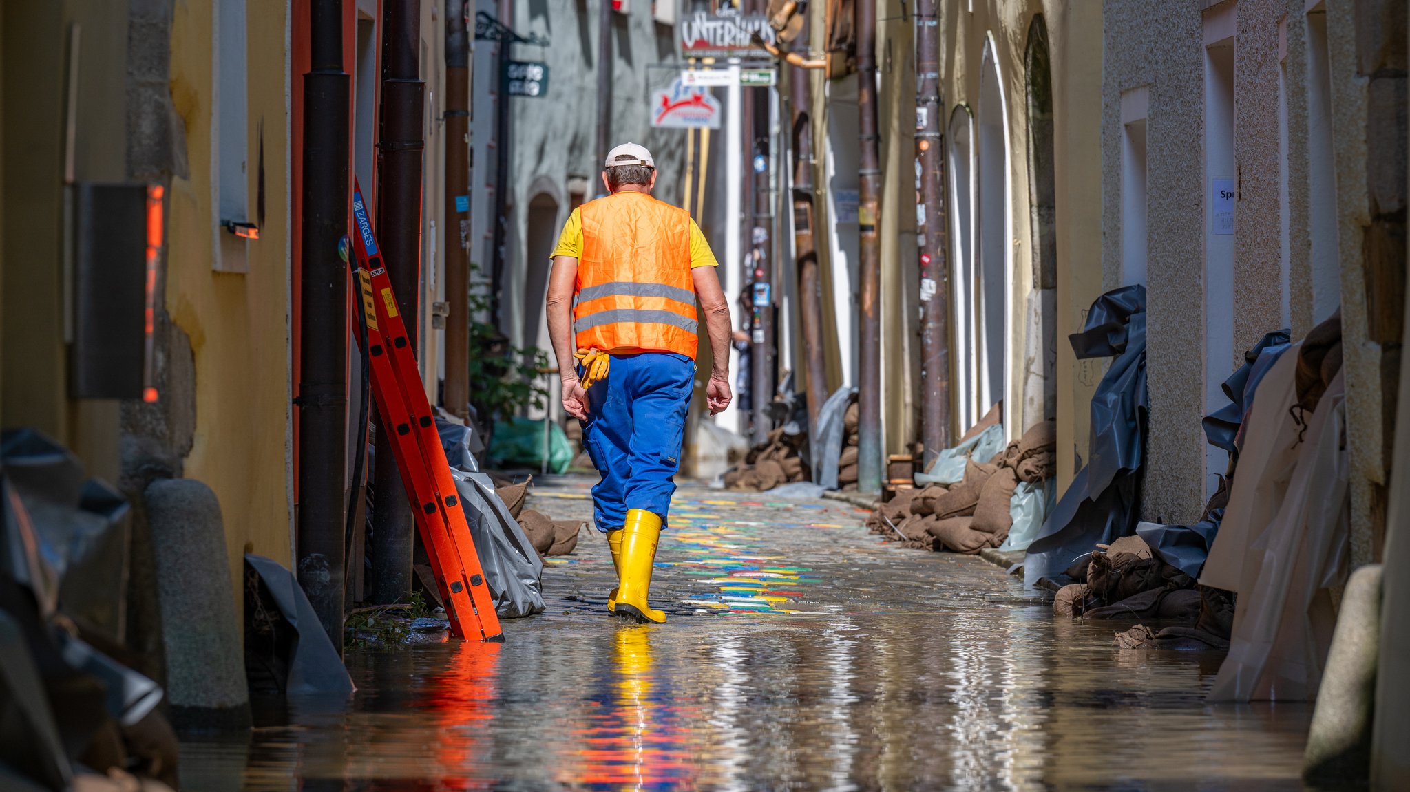 Archivbild: Ein Helfer geht, nachdem das Hochwasser der Donau etwas zurückgegangen ist, durch eine Gasse mit Sandsäcken vor den Häusern.